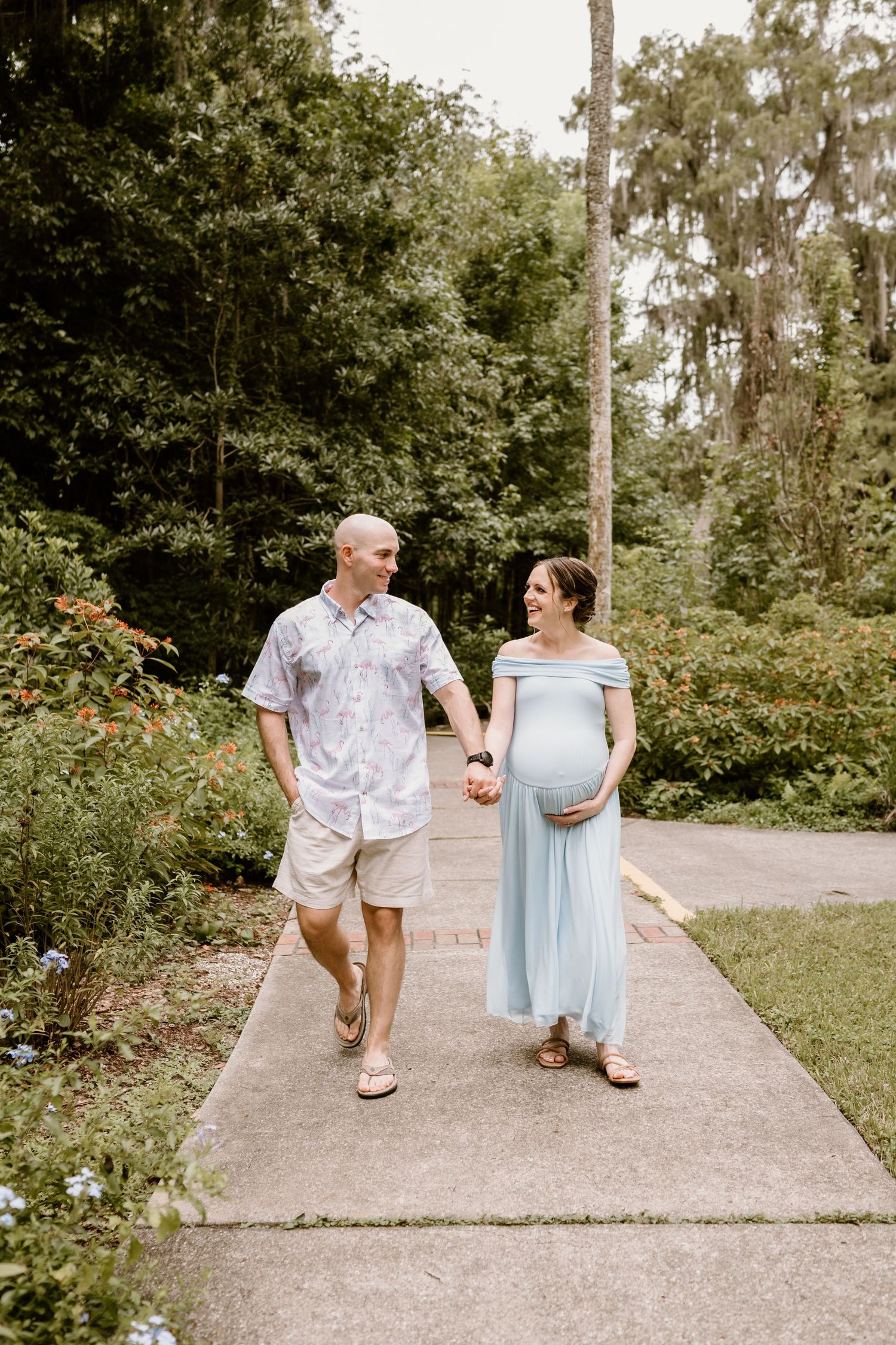 Couple strolling down garden pathway during maternity photo session.