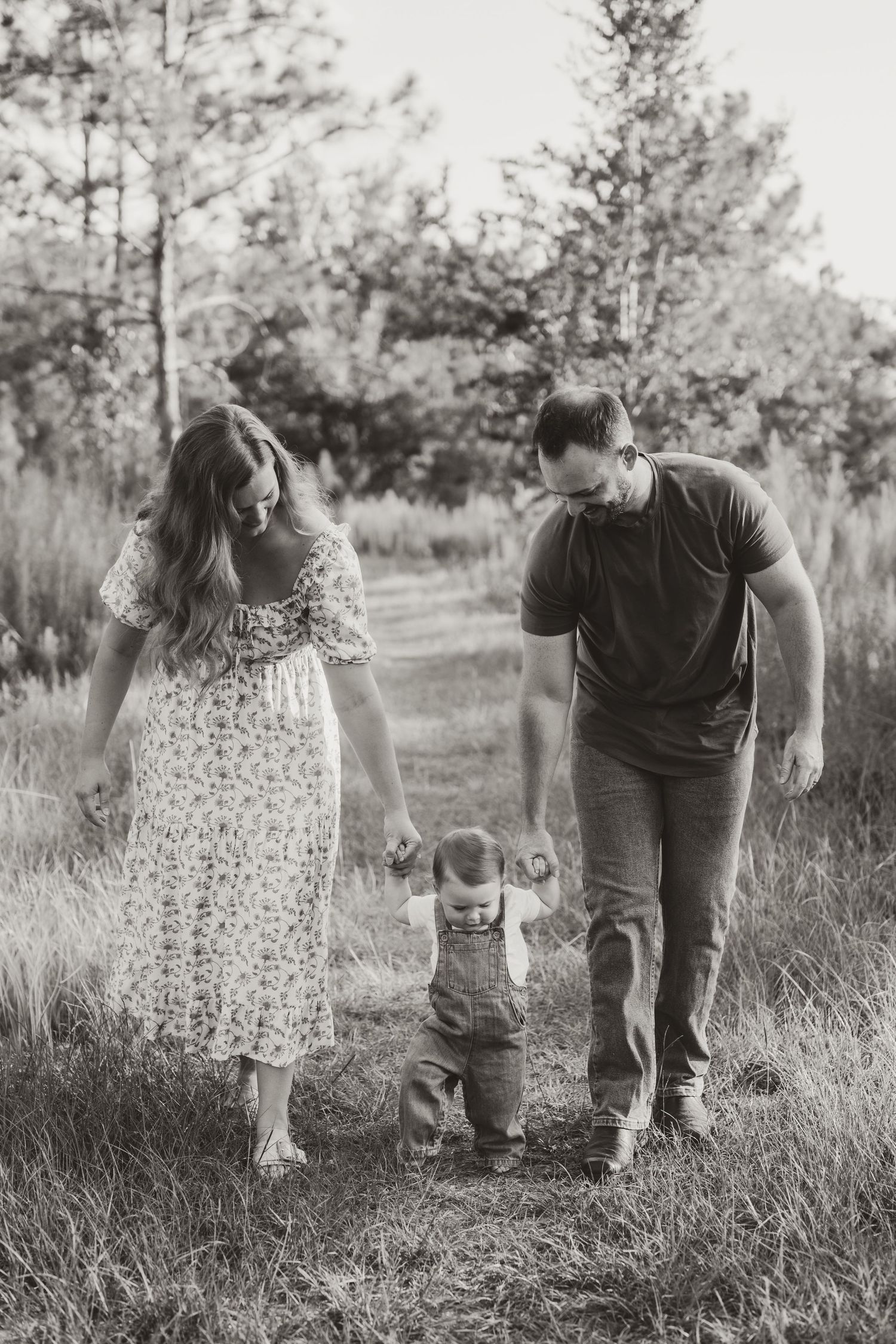 Black and white photo of a family walking together through a grassy field holding hands.