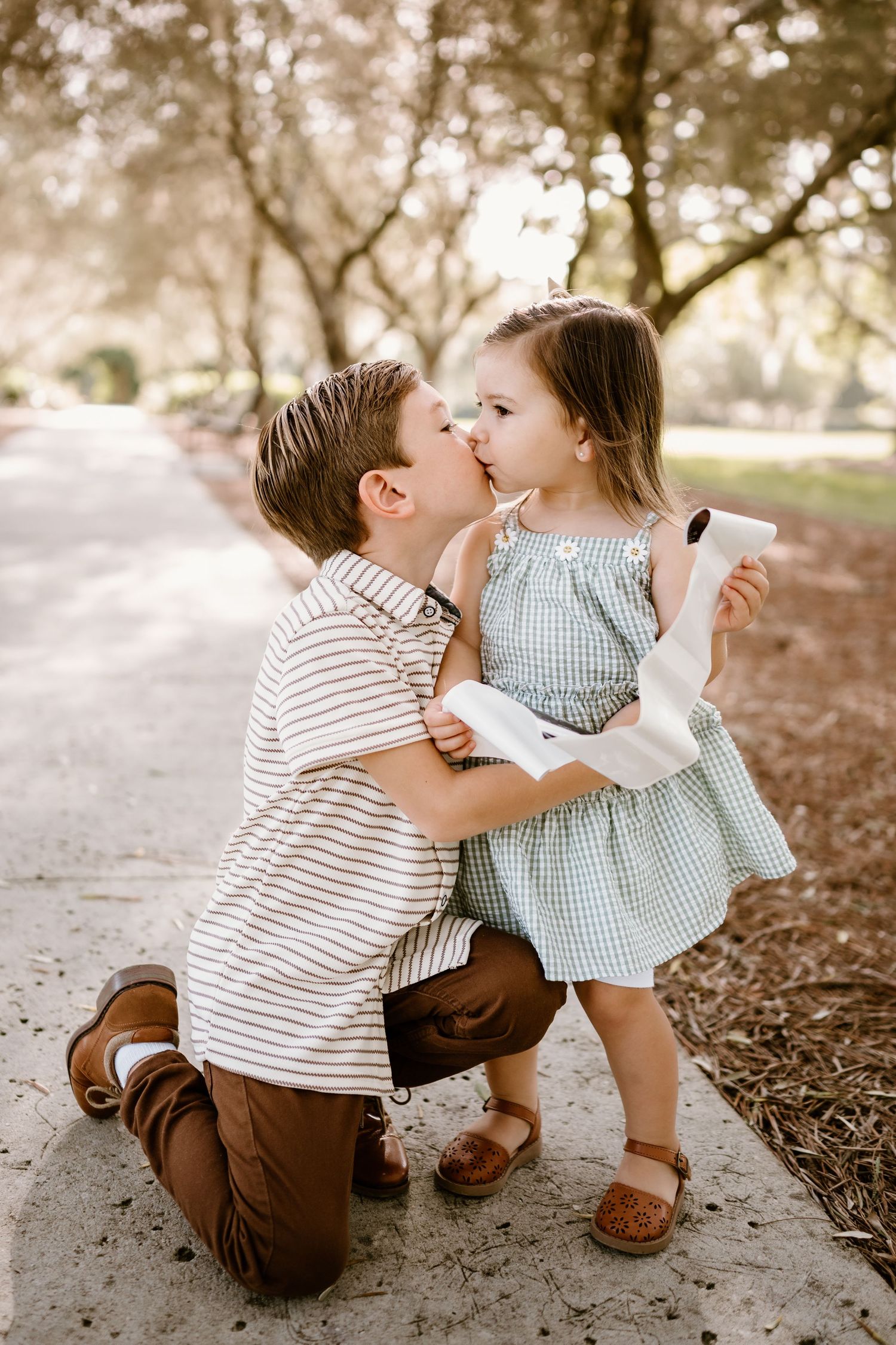Tender interaction between young children under a tree with soft lighting.