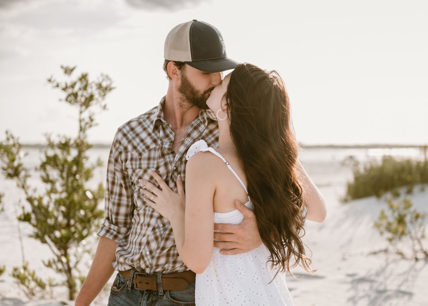 A romantic beach photoshoot featuring a couple embracing against a bright coastal backdrop.
