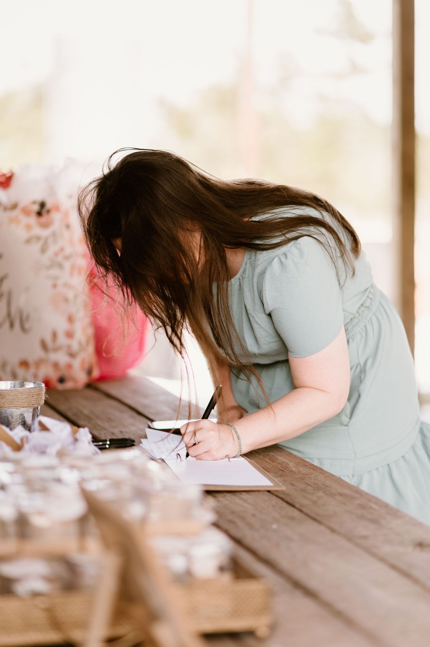 Person in light blue dress writing in a journal at wooden table.