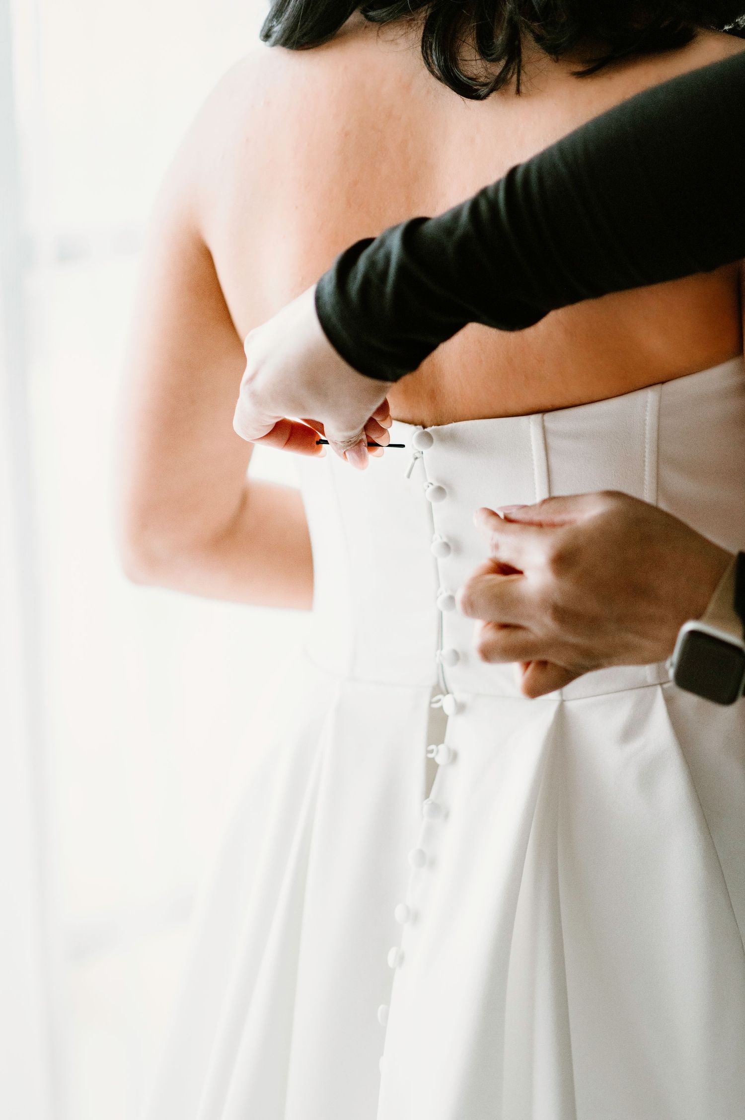 Hands helping to button up the back of a white wedding dress.