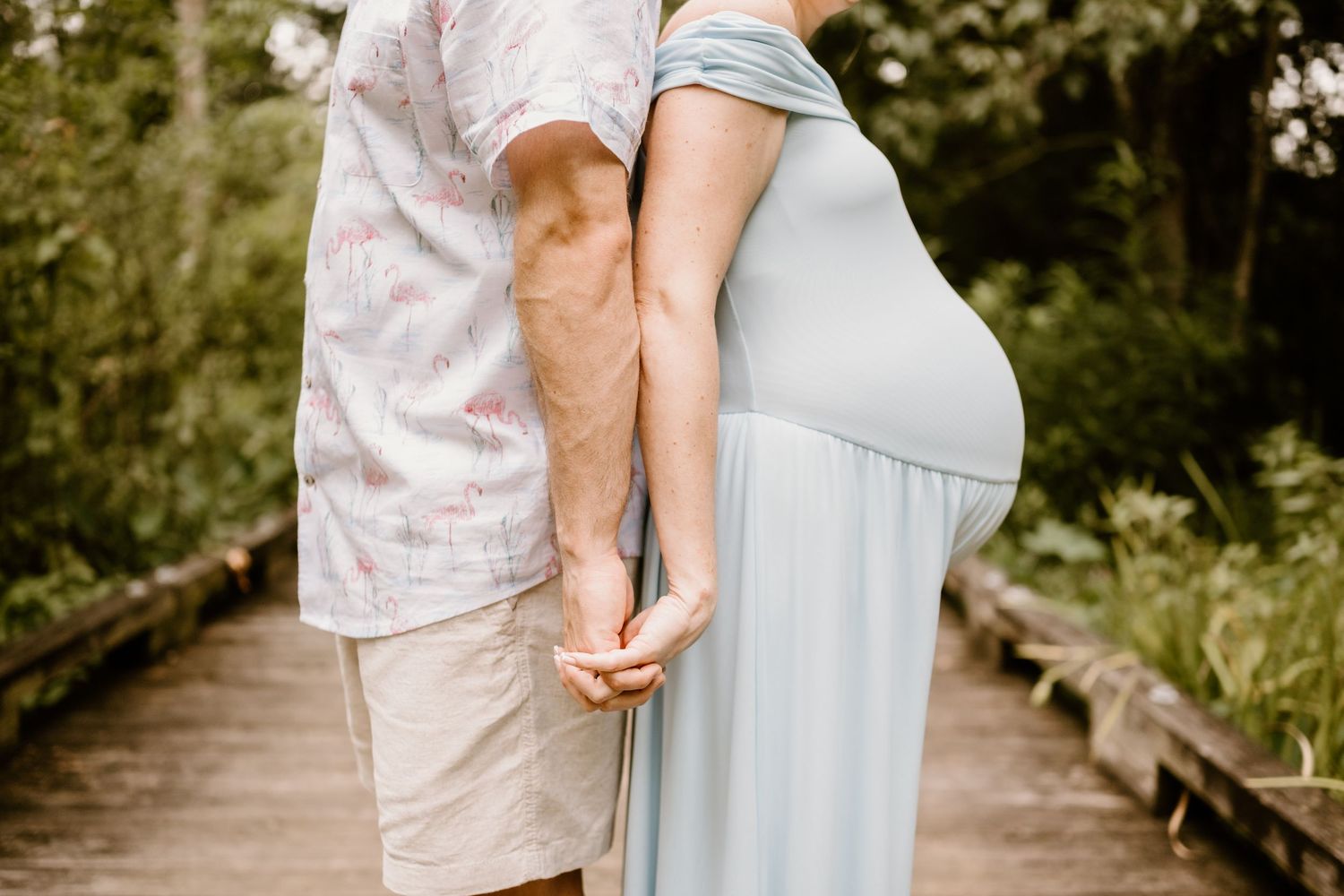Couple holds hands during romantic maternity photoshoot in garden setting.