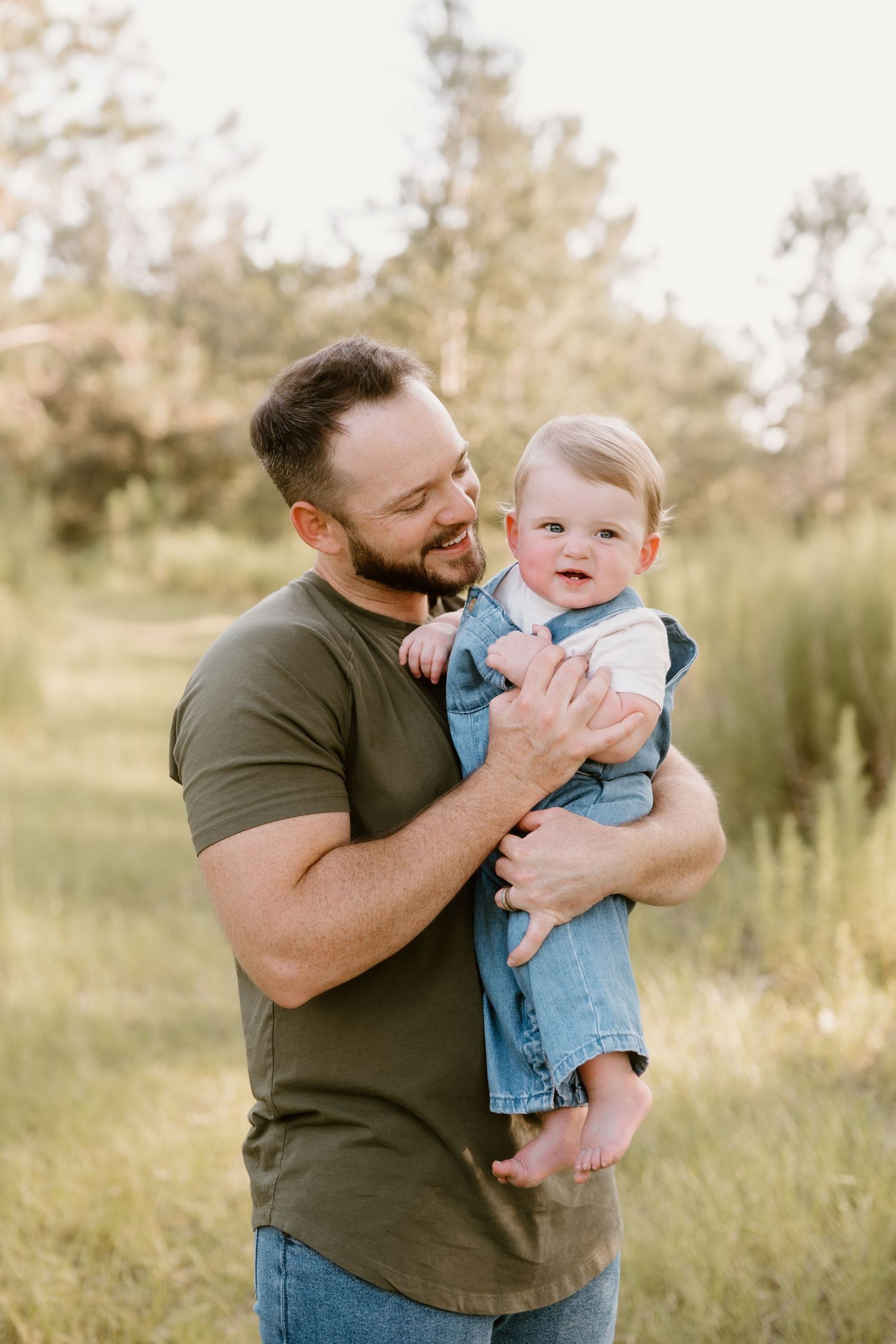 A tender moment between parent and baby in a sunny field with tall grass.