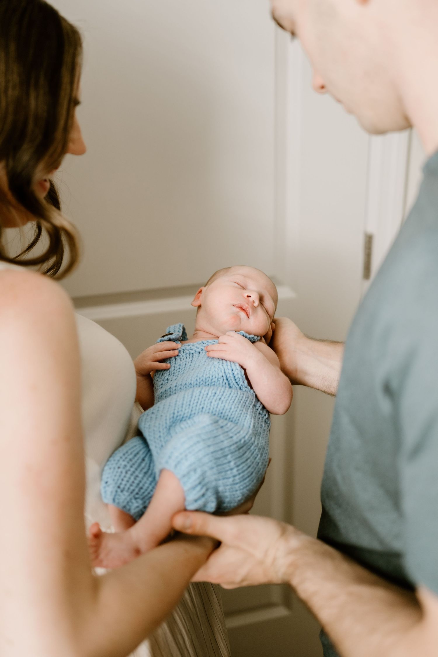 Gentle hands cradle a sleeping baby wearing a light blue knitted romper.