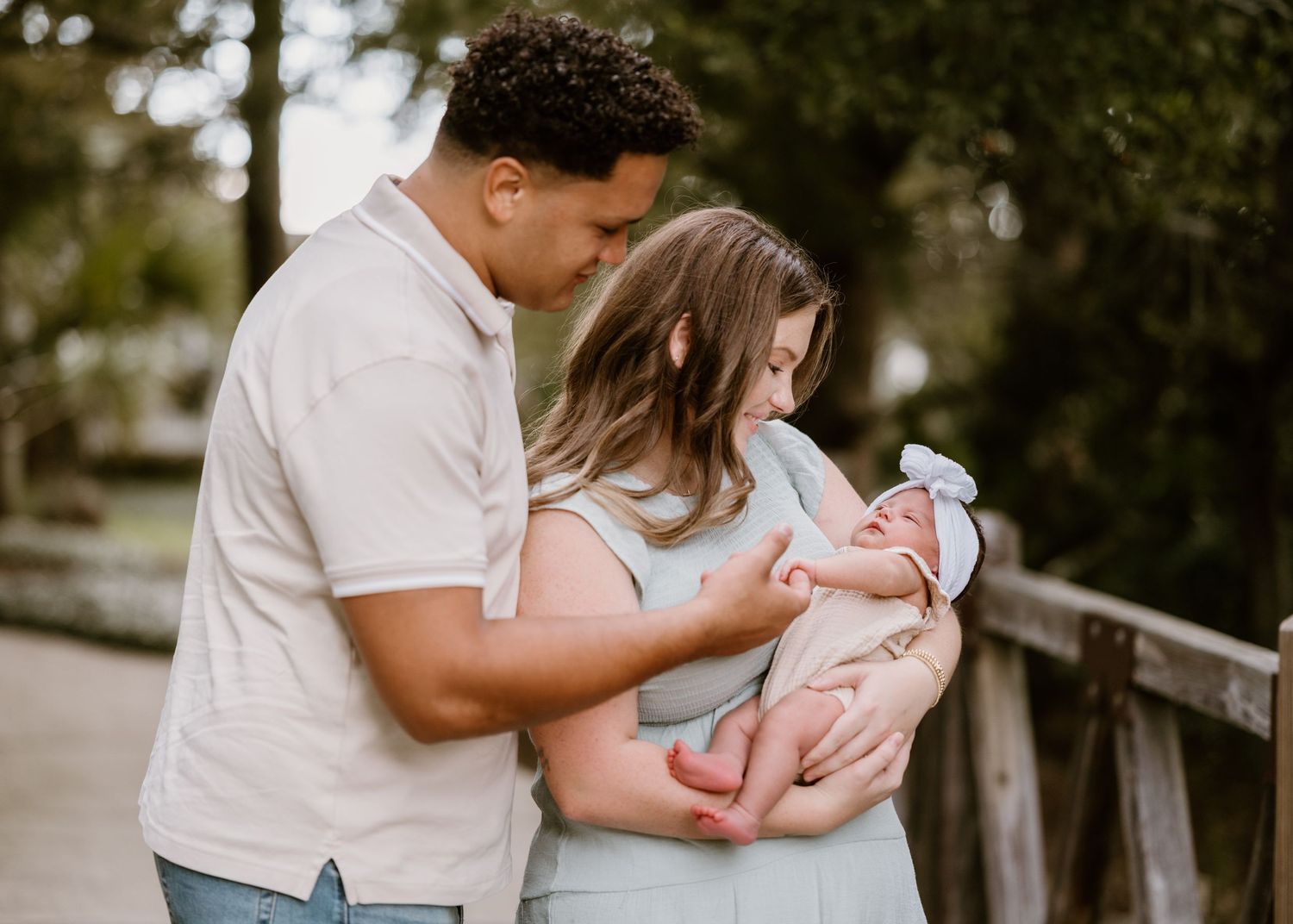 New parents share tender moments with their newborn baby outdoors on a blanket in natural lighting.