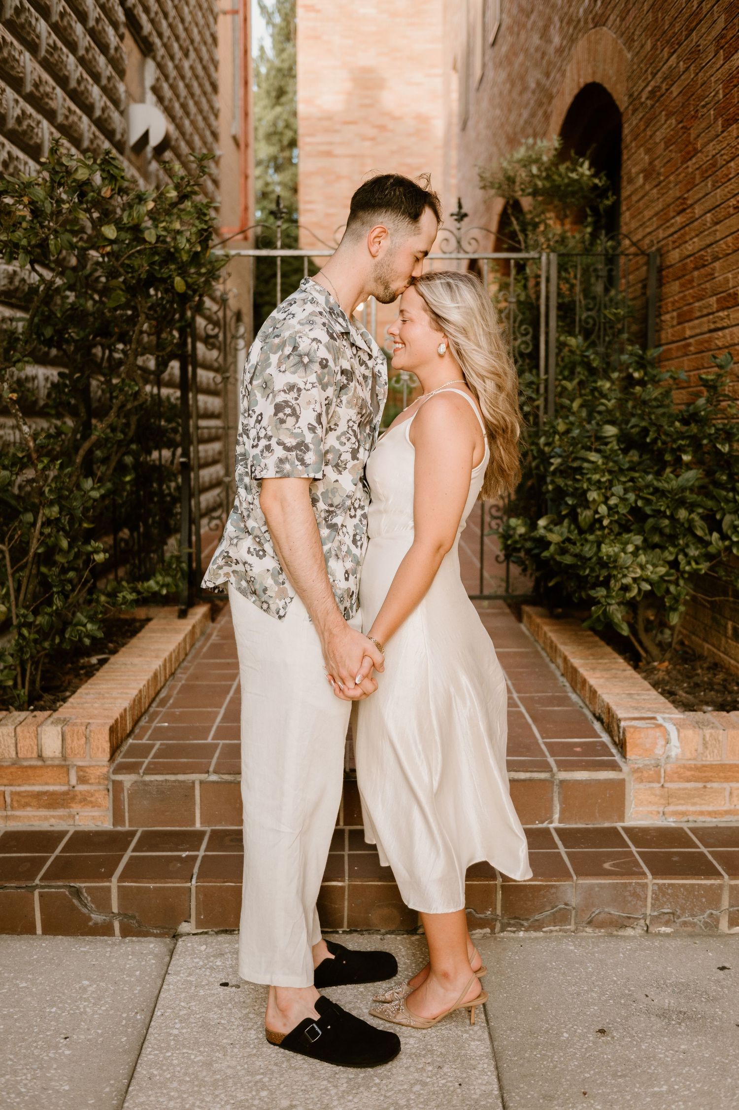 A couple shares romantic moments during an engagement session near a brick wall.