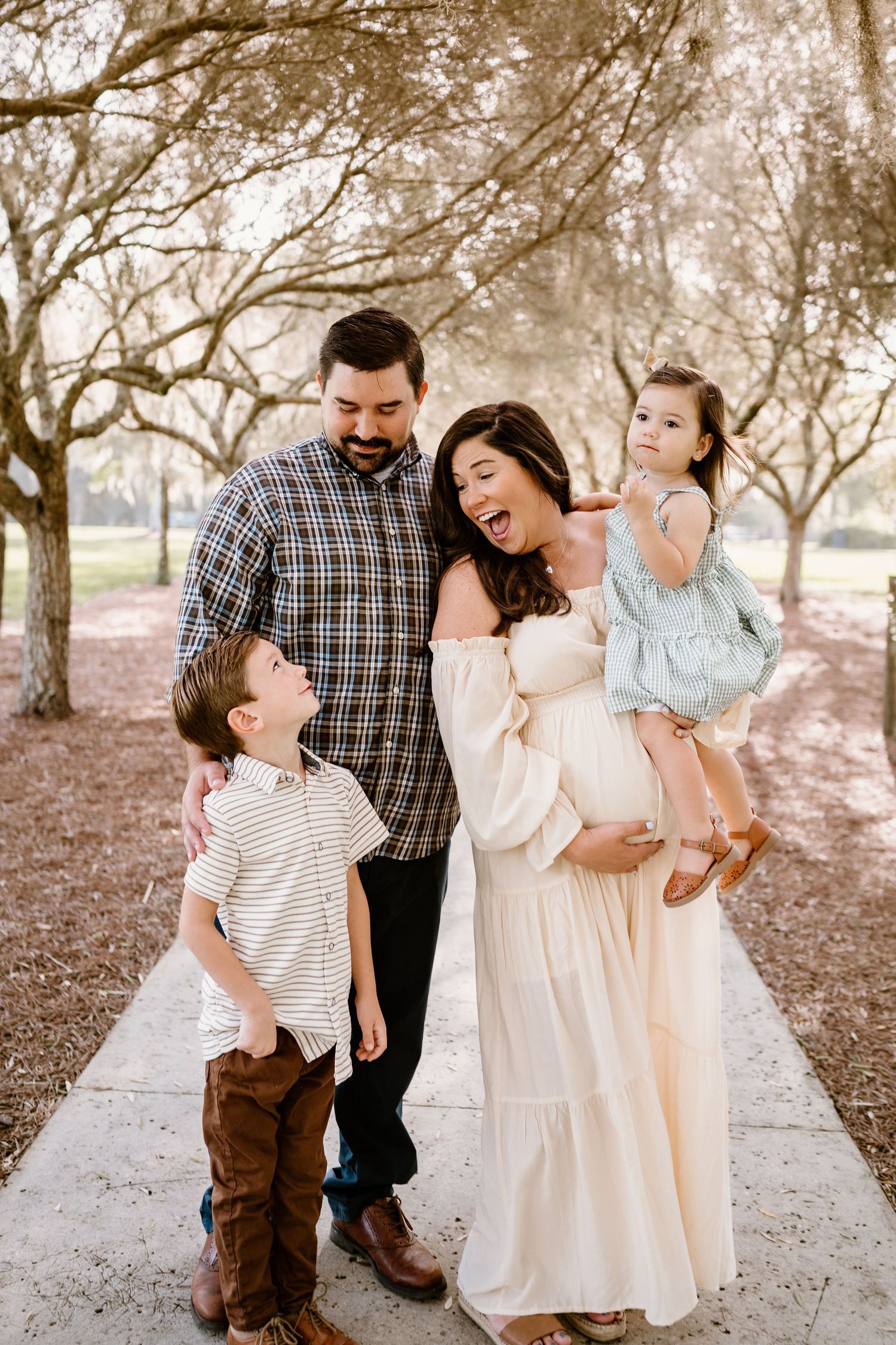 Family shares joyful candid moments together on tree-lined path during outdoor photo session.