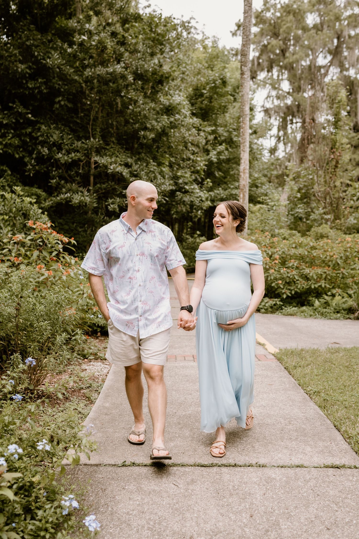 Expectant couple walking on path through lush garden setting.