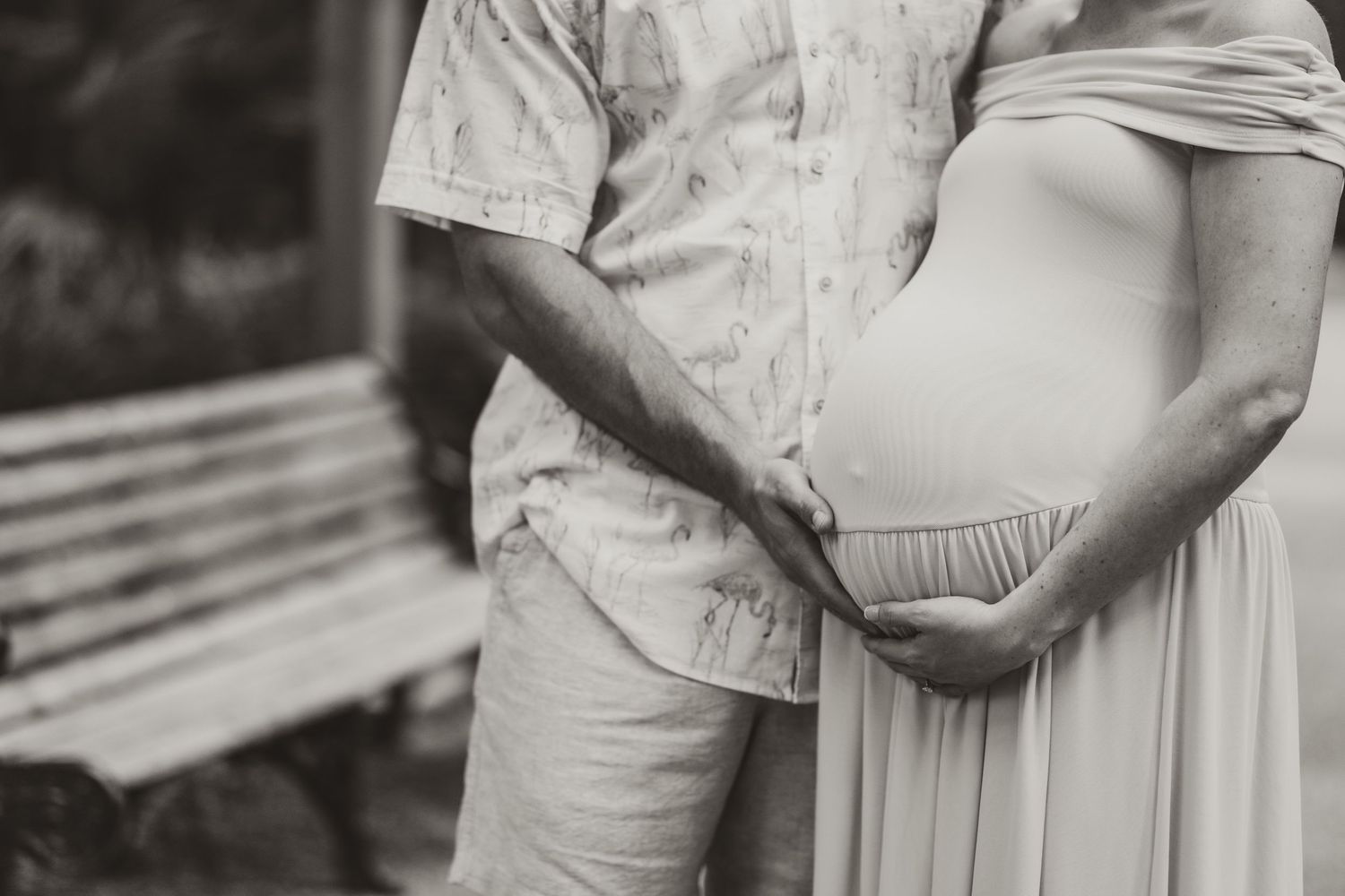 Black and white close-up of a pregnant belly being held by a couple in casual attire.