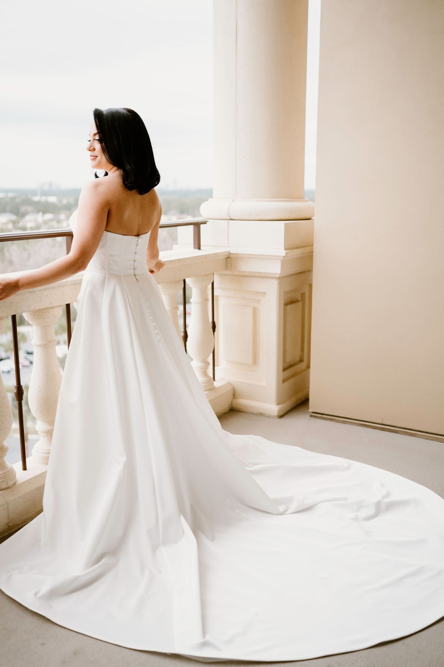 Flowing white wedding dress with dramatic train photographed against beige walls and railing.