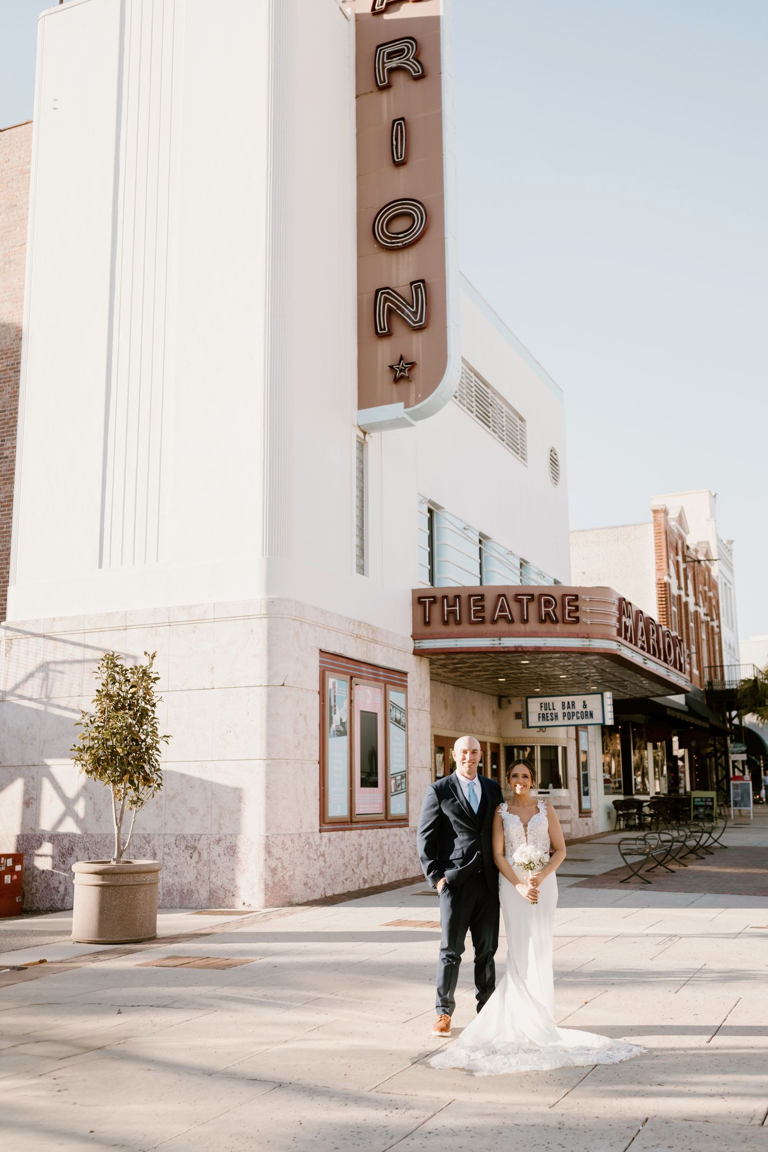 Artistic wedding portraits taken outside retro theater building in bright daylight.