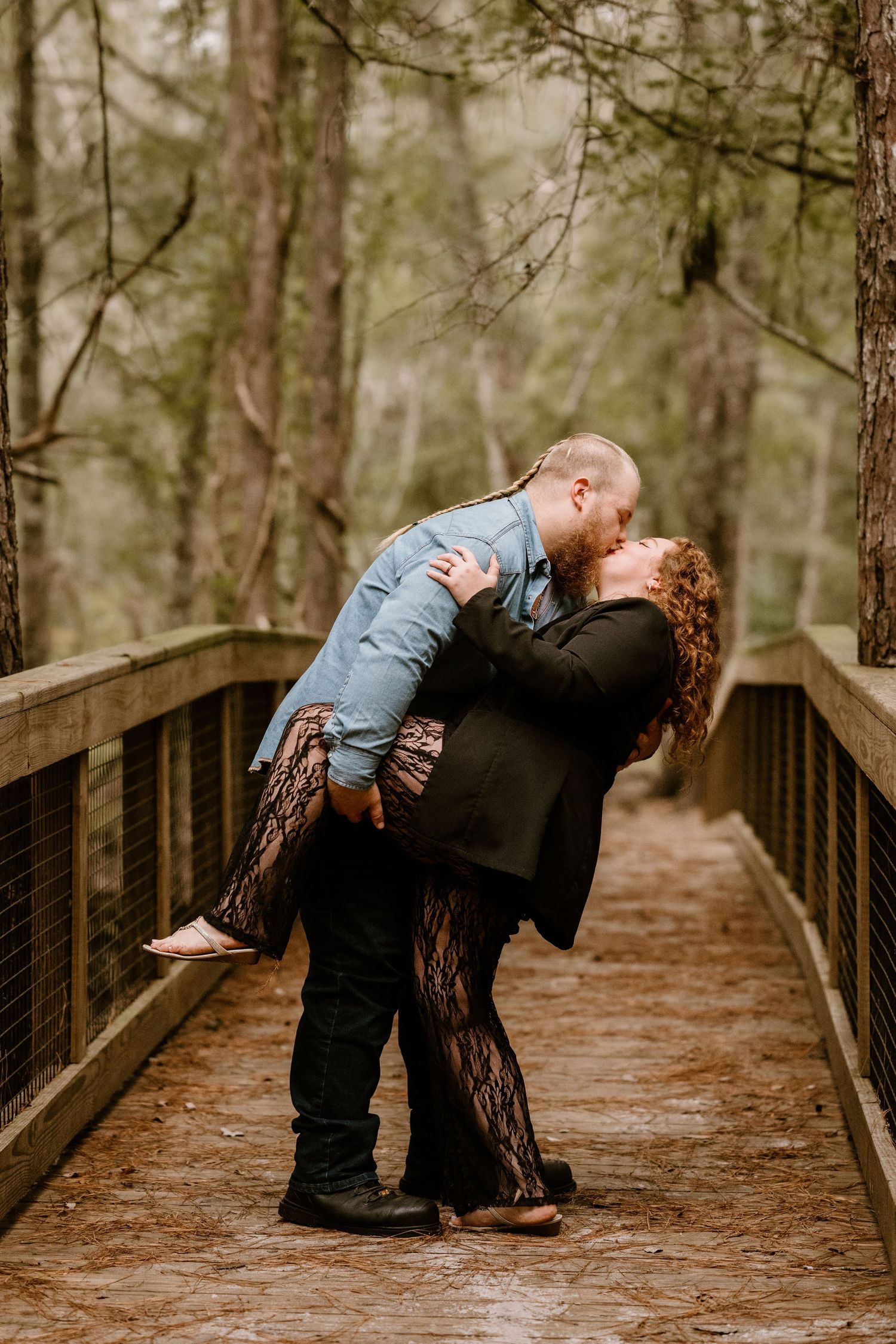 Couple sharing romantic pose on wooden bridge in forest setting.