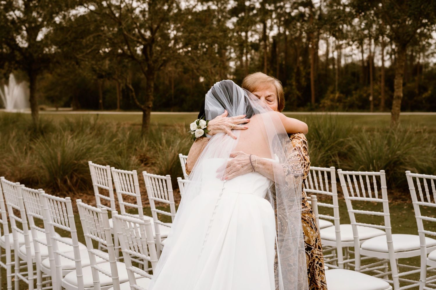 White ceremony chairs lined up outdoors with trees creating a natural backdrop.