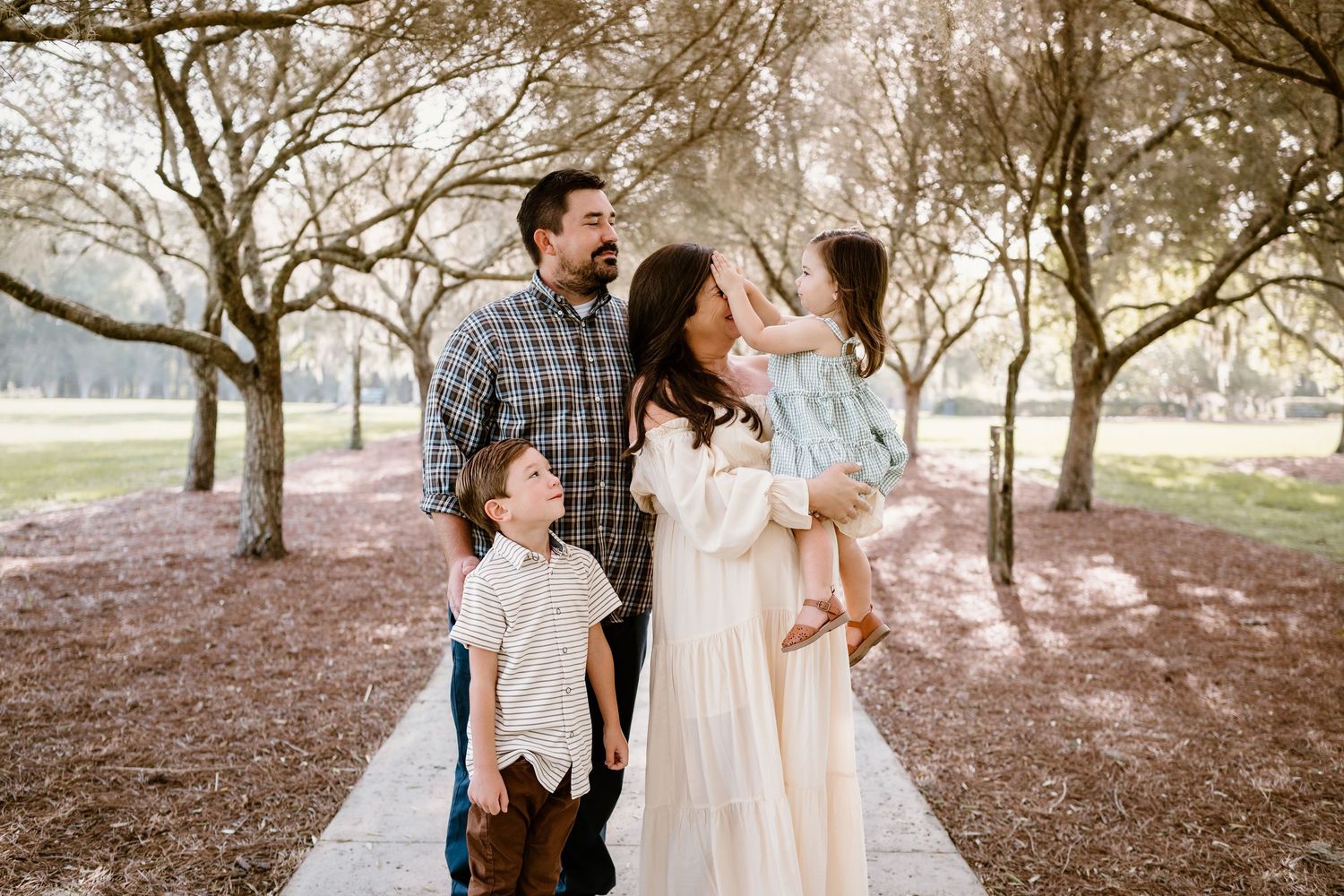 Family walking together under a canopy of trees in a park setting.