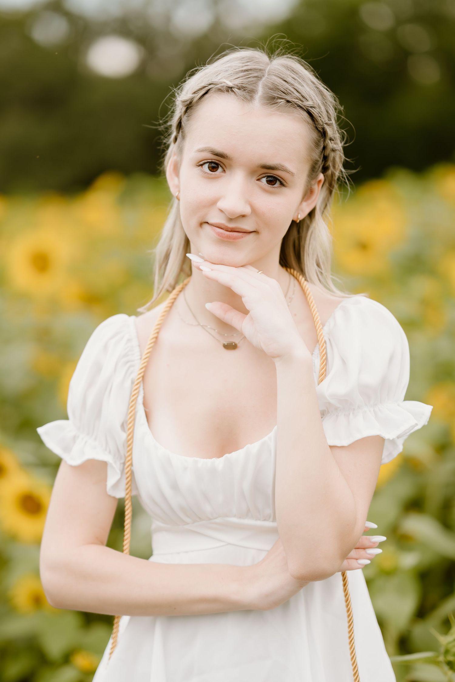 Young person in white dress poses playfully in a sunflower field on a sunny day.
