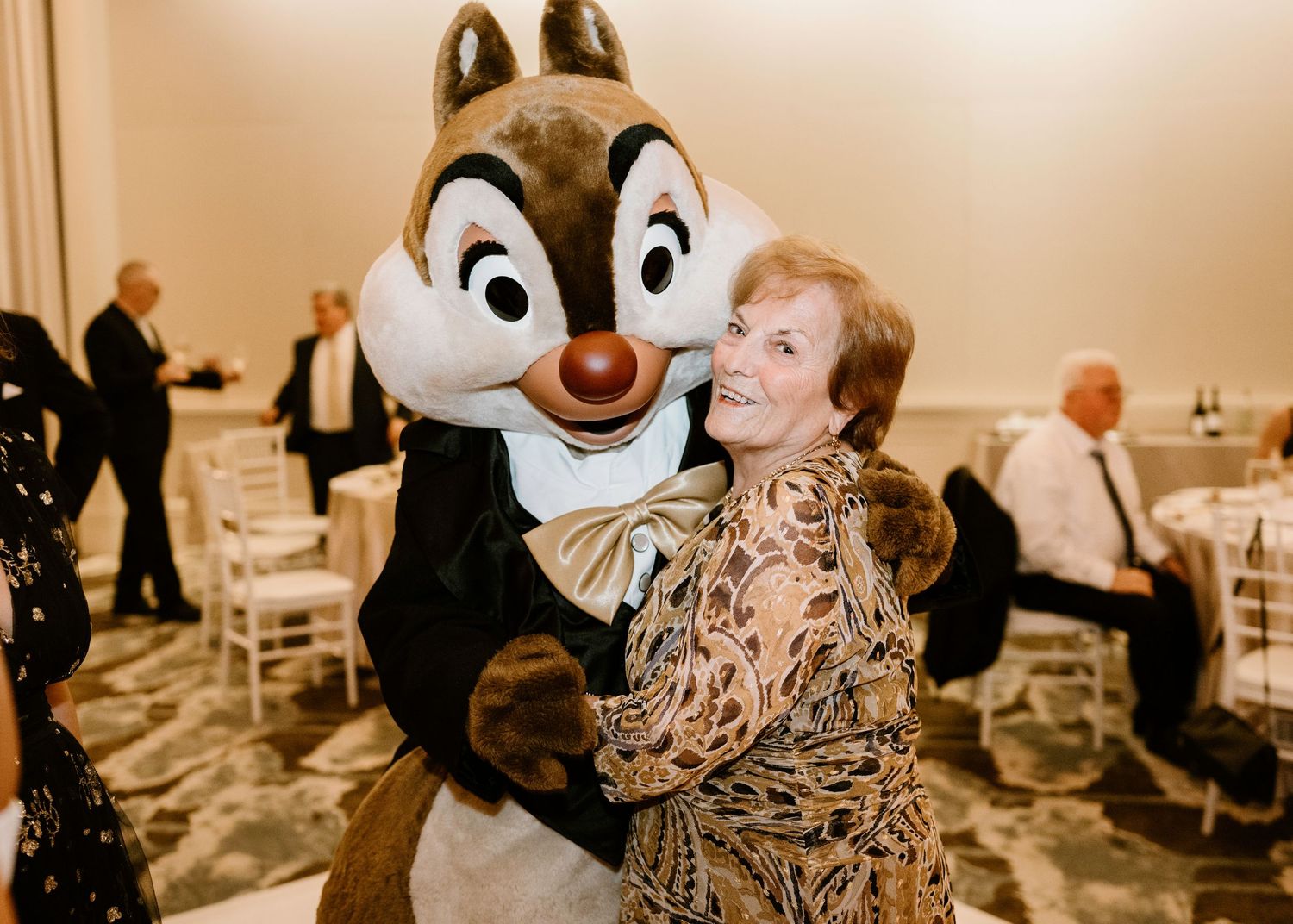 Disney chipmunk character mascot interacts with wedding guests in formal attire.
