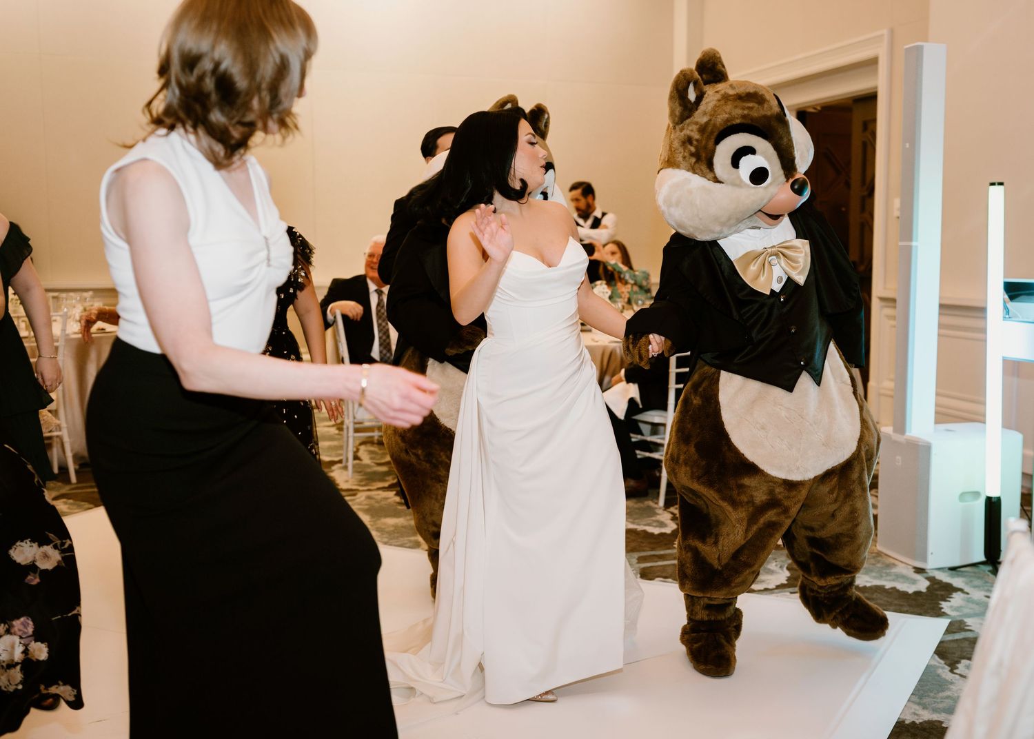 Wedding guests dance with Disney chipmunk characters during a reception celebration.