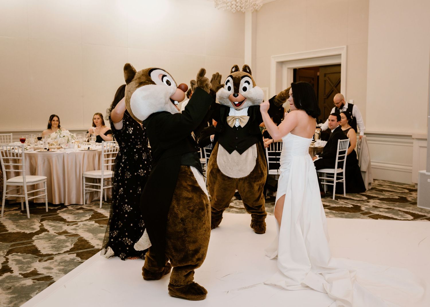 Disney mascot characters dance with wedding guests in an elegant ballroom setting.