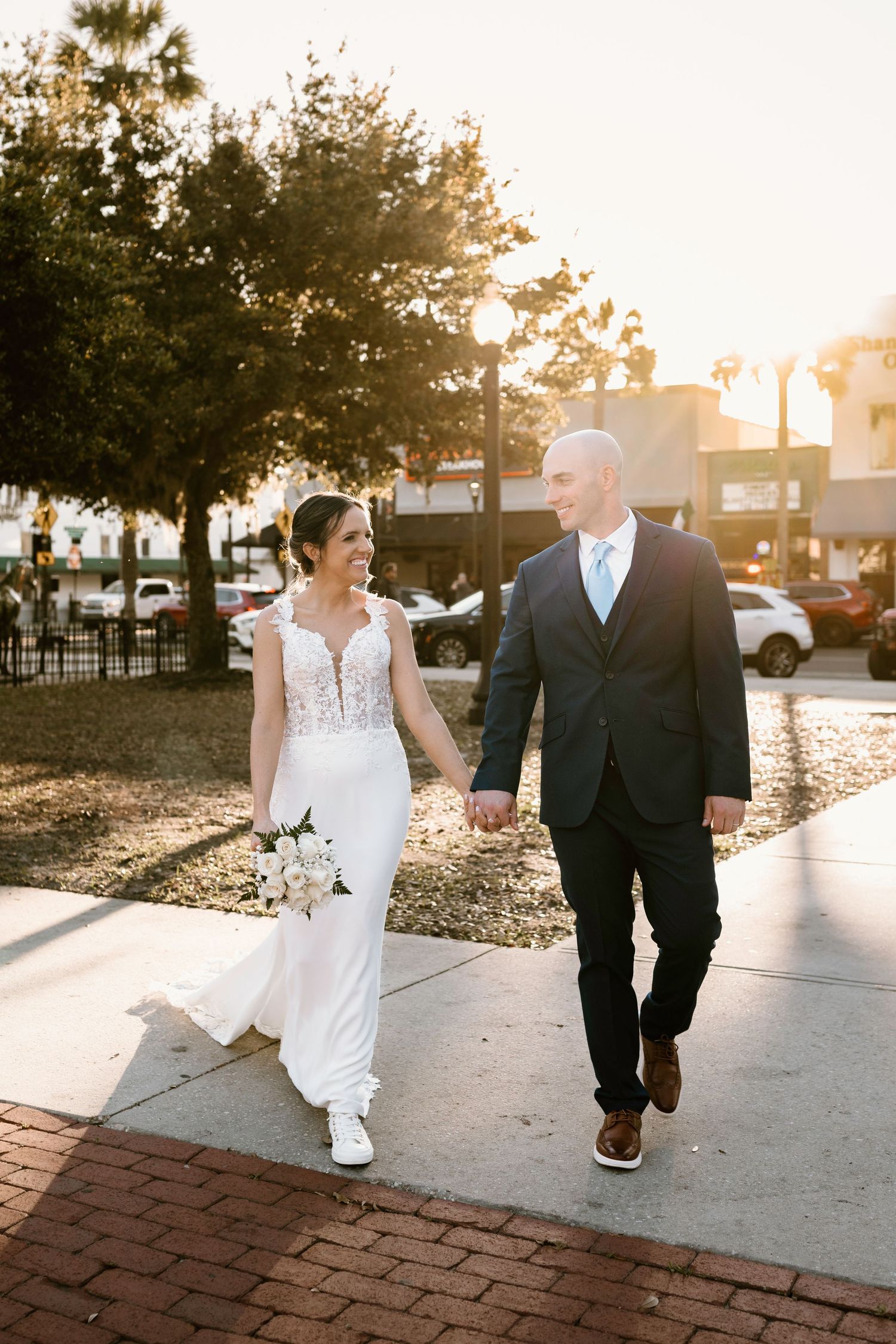 Wedding couple walking together at sunset on brick pathway with trees in background.