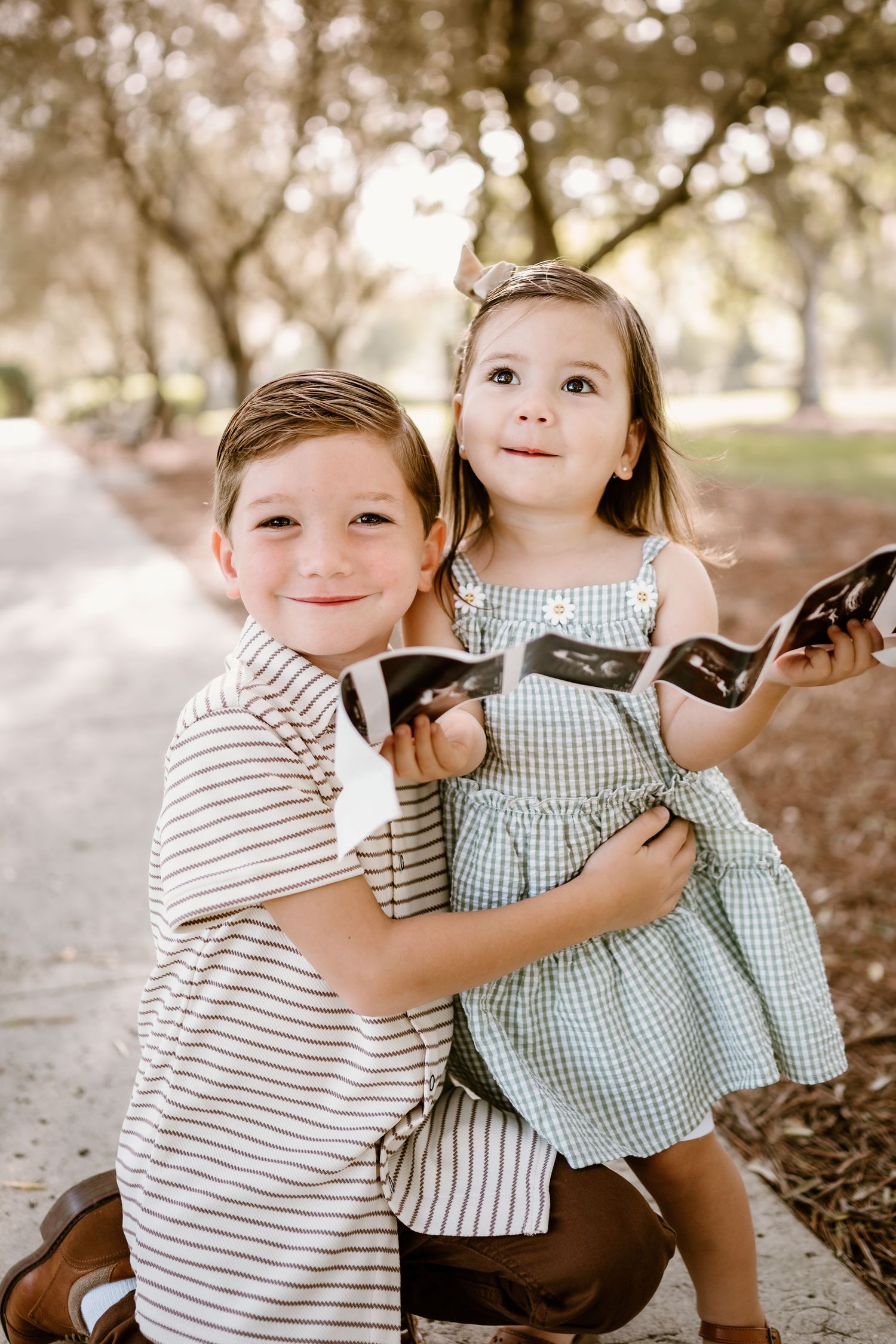 Two young children play and laugh together while sitting on fallen leaves.
