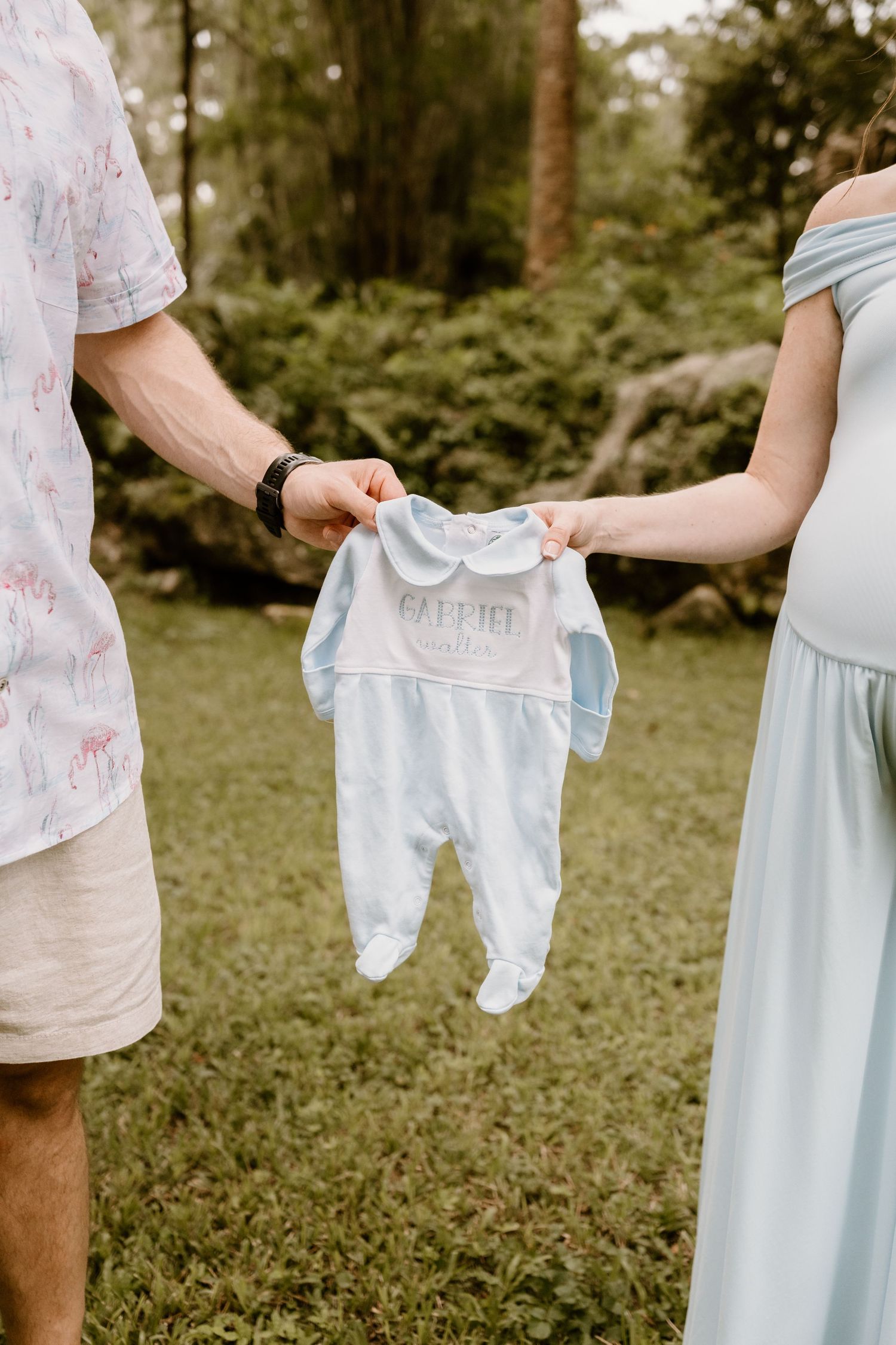 Couple holding up tiny baby clothes during pregnancy announcement photoshoot.