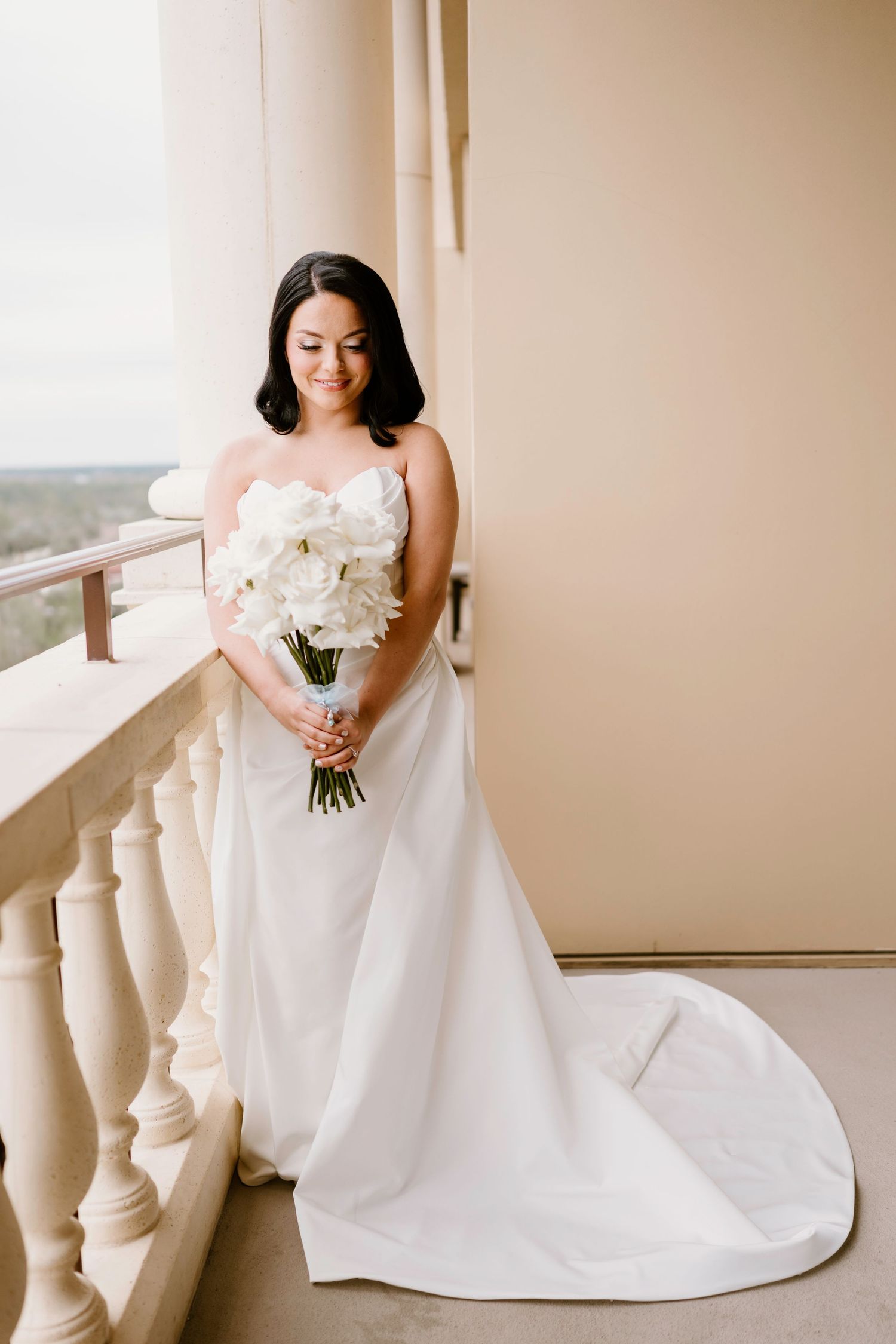 Elegant white wedding gown with a sweetheart neckline and white floral bouquet against a neutral backdrop.