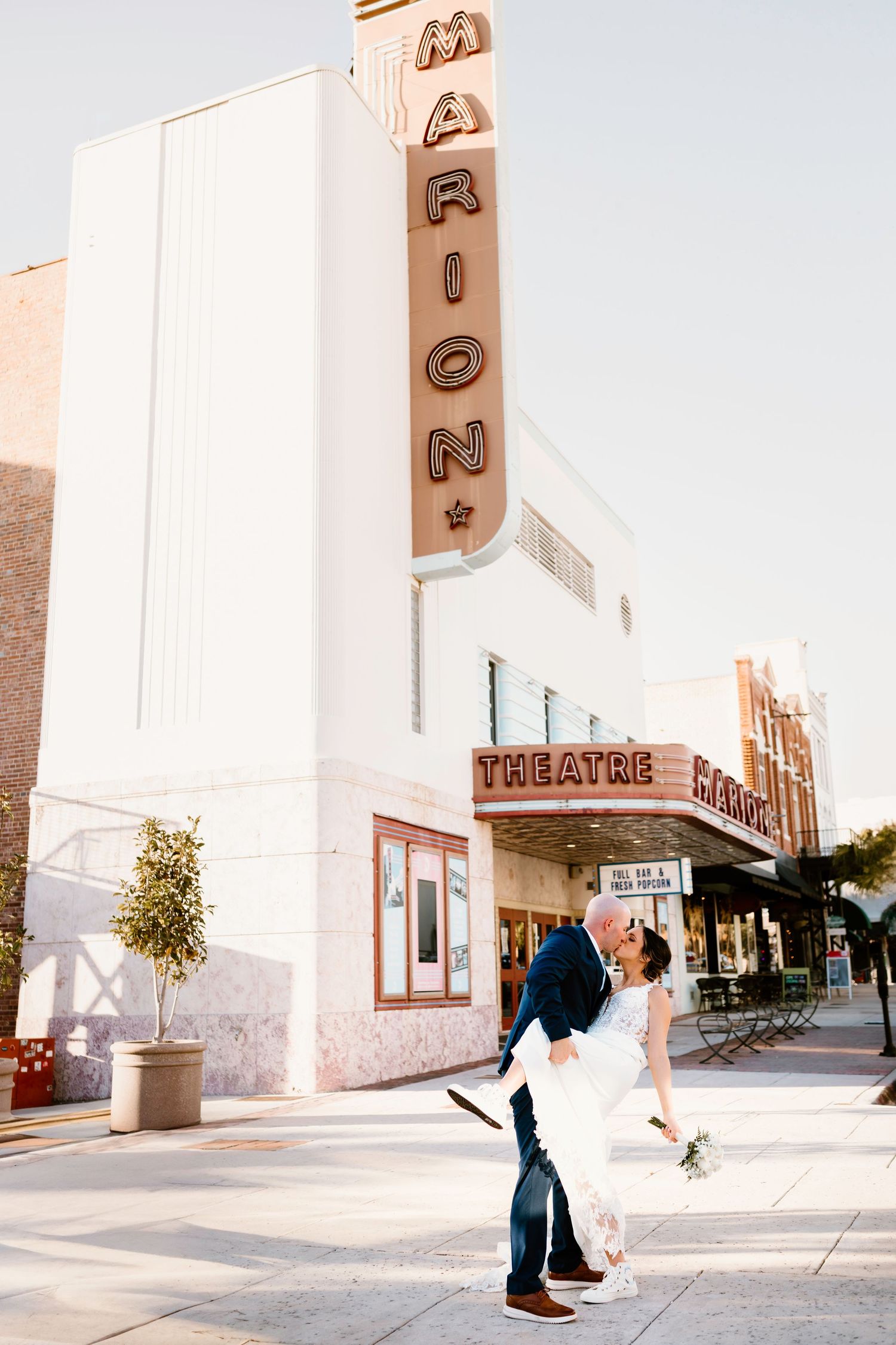 Wedding couple poses playfully outside vintage theater with art deco architecture.