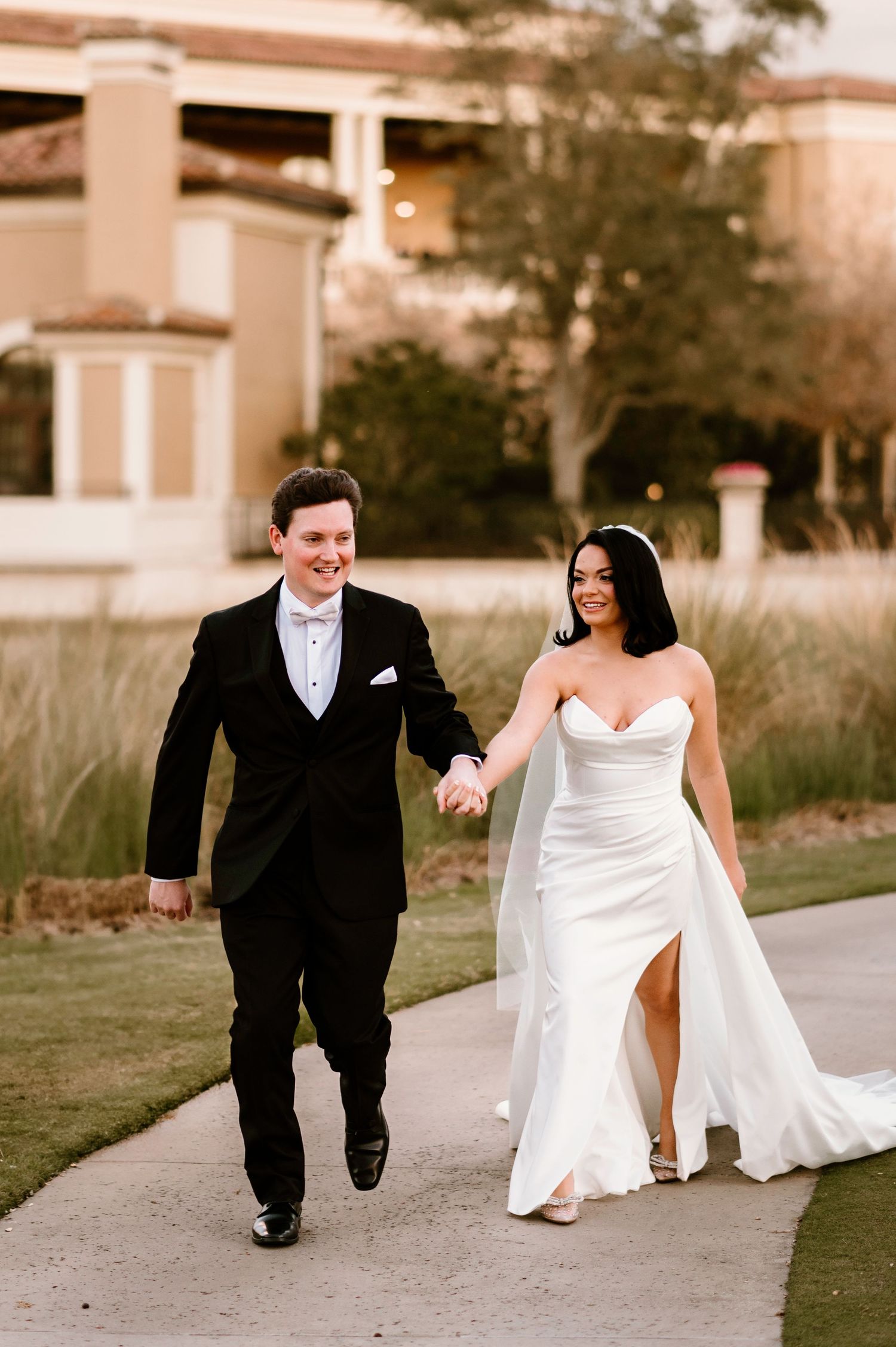 Newlyweds share playful moment walking together on garden path at luxury resort.