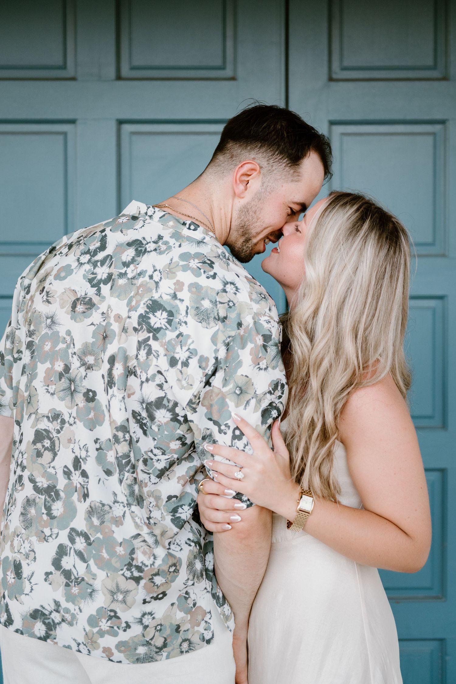 A couple shares intimate moments during an engagement photoshoot against a blue door.