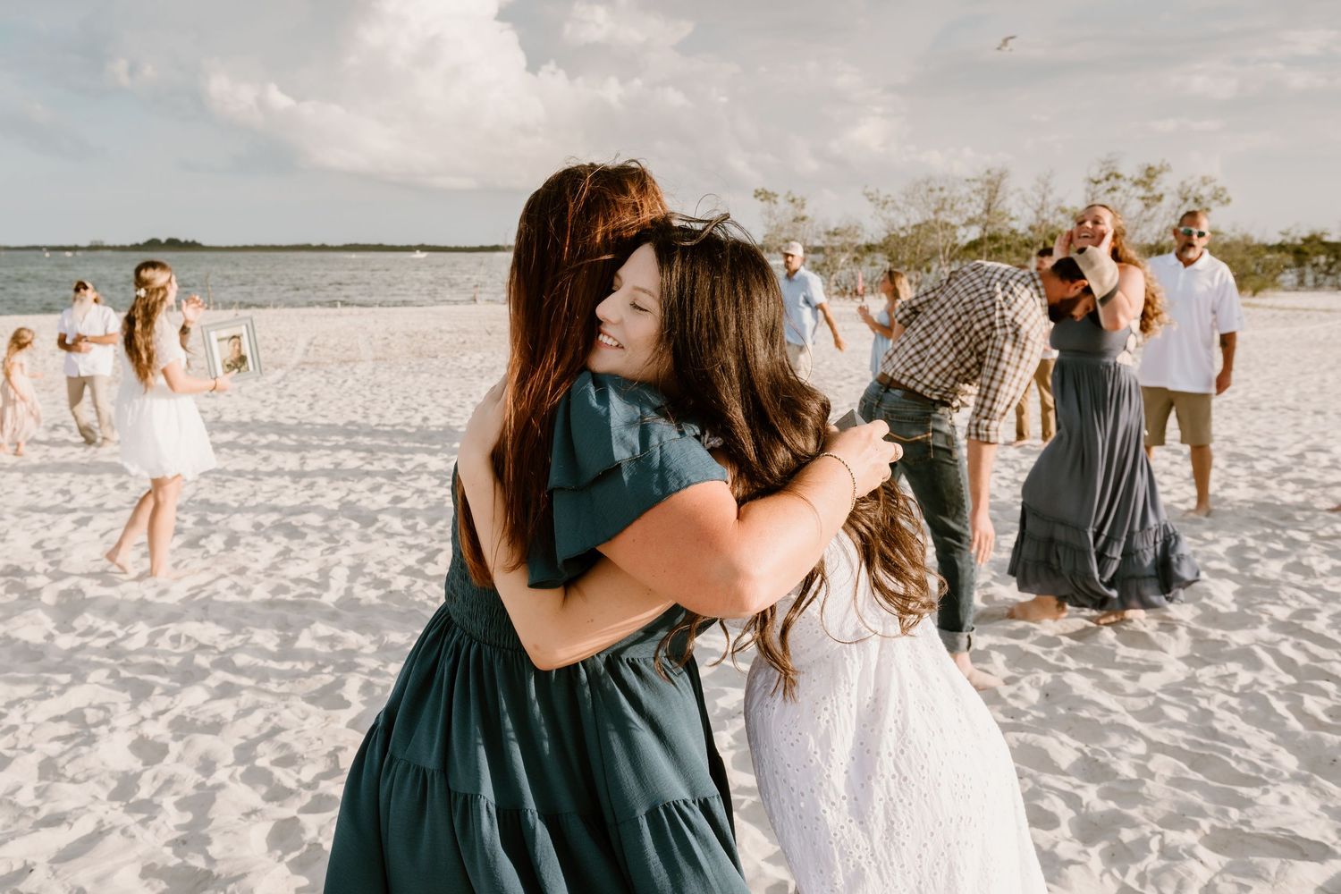 A group gathers for candid photos on a sunny beach with white sand and blue skies.