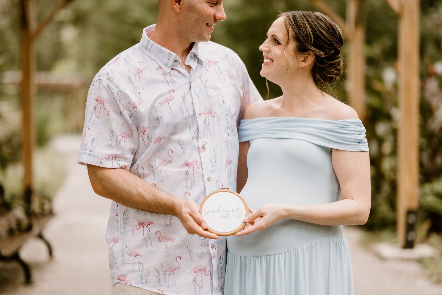 Romantic couple poses together in a sunlit outdoor setting wearing pastel colors.