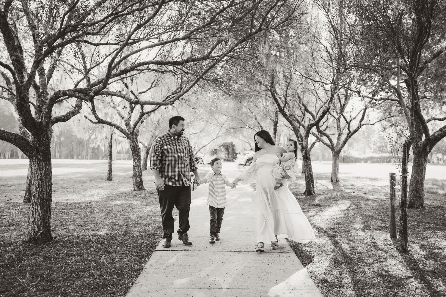Family walking together on a tree-lined path in black and white photography.
