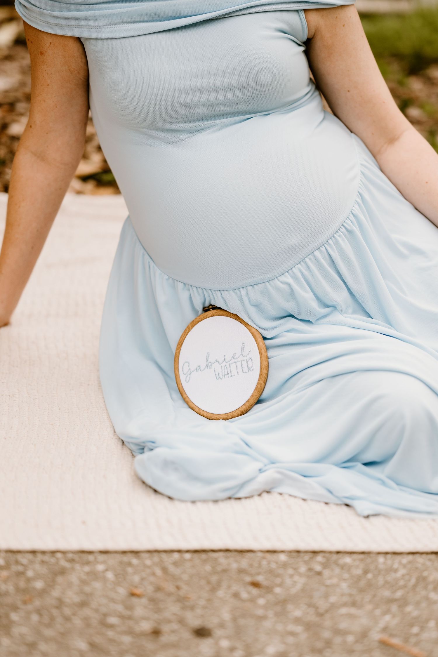 Close-up of a wooden embroidery hoop holding light blue fabric against a stone surface.