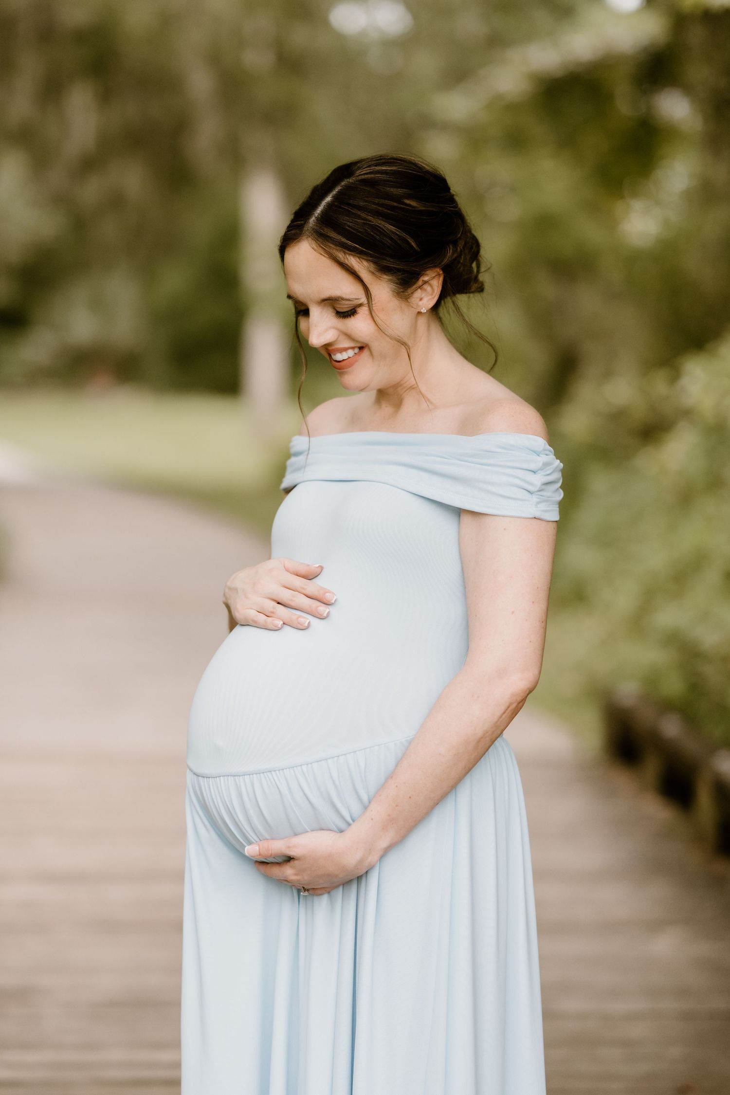 Expectant mother in pale blue dress holding her baby bump in outdoor maternity photos.