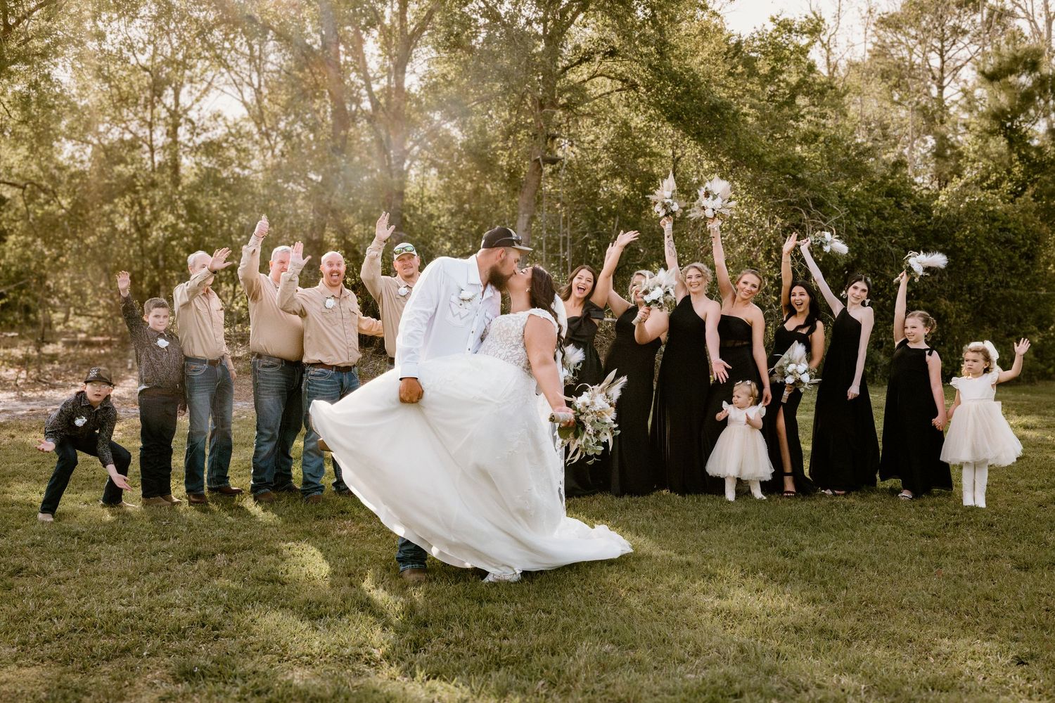 Wedding party and guests celebrate with fun group photo on grassy lawn during reception.