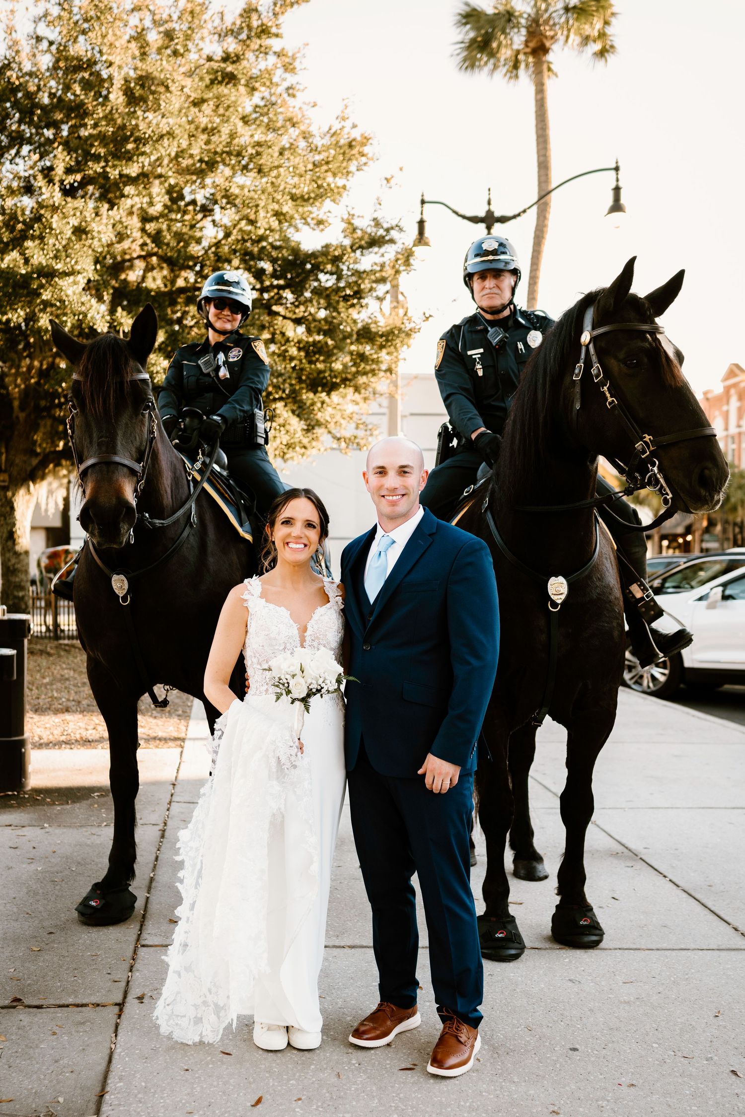 Wedding couple poses with mounted police officers and their horses on a city street.