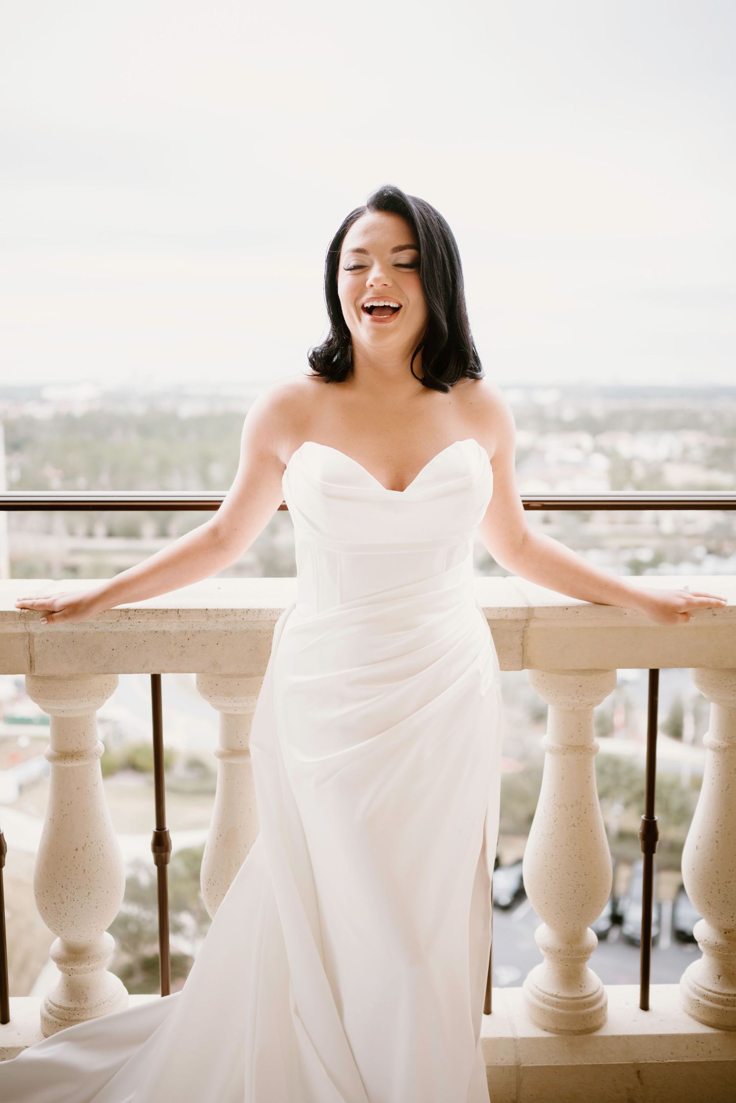 Joyful bridal moment captured on an elegant balcony with white stone columns.