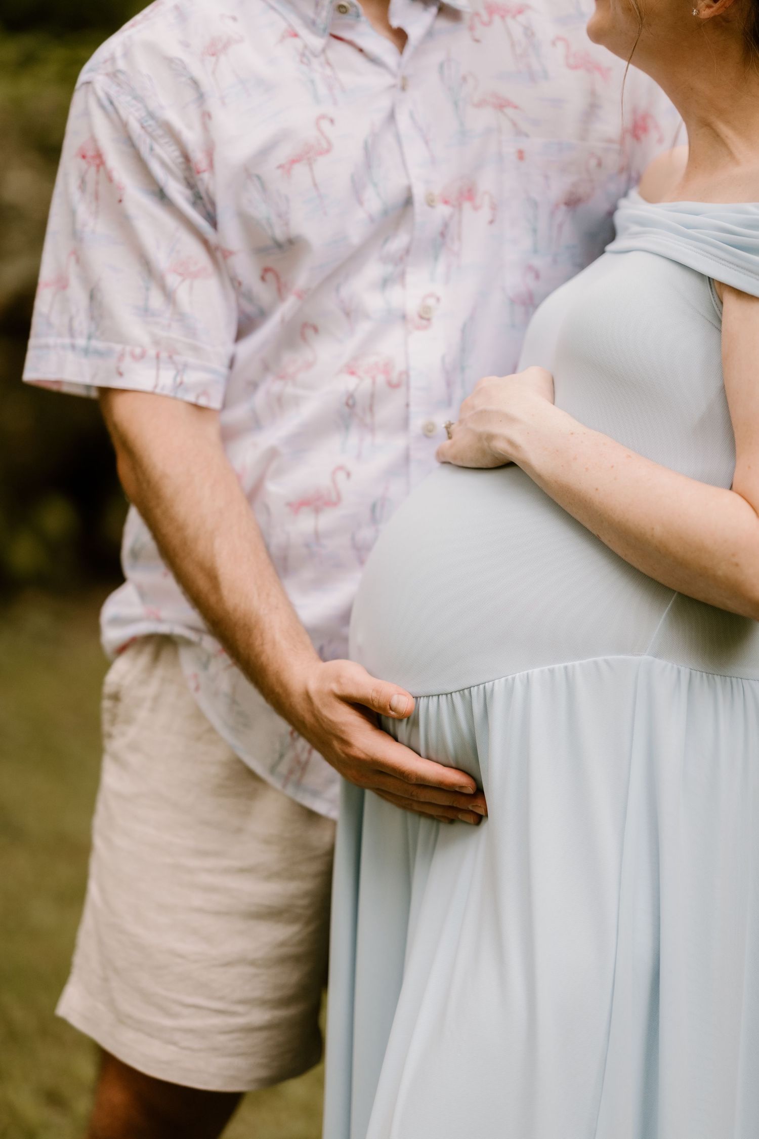 Close-up of couple's hands on pregnant belly wearing light blue maternity dress.