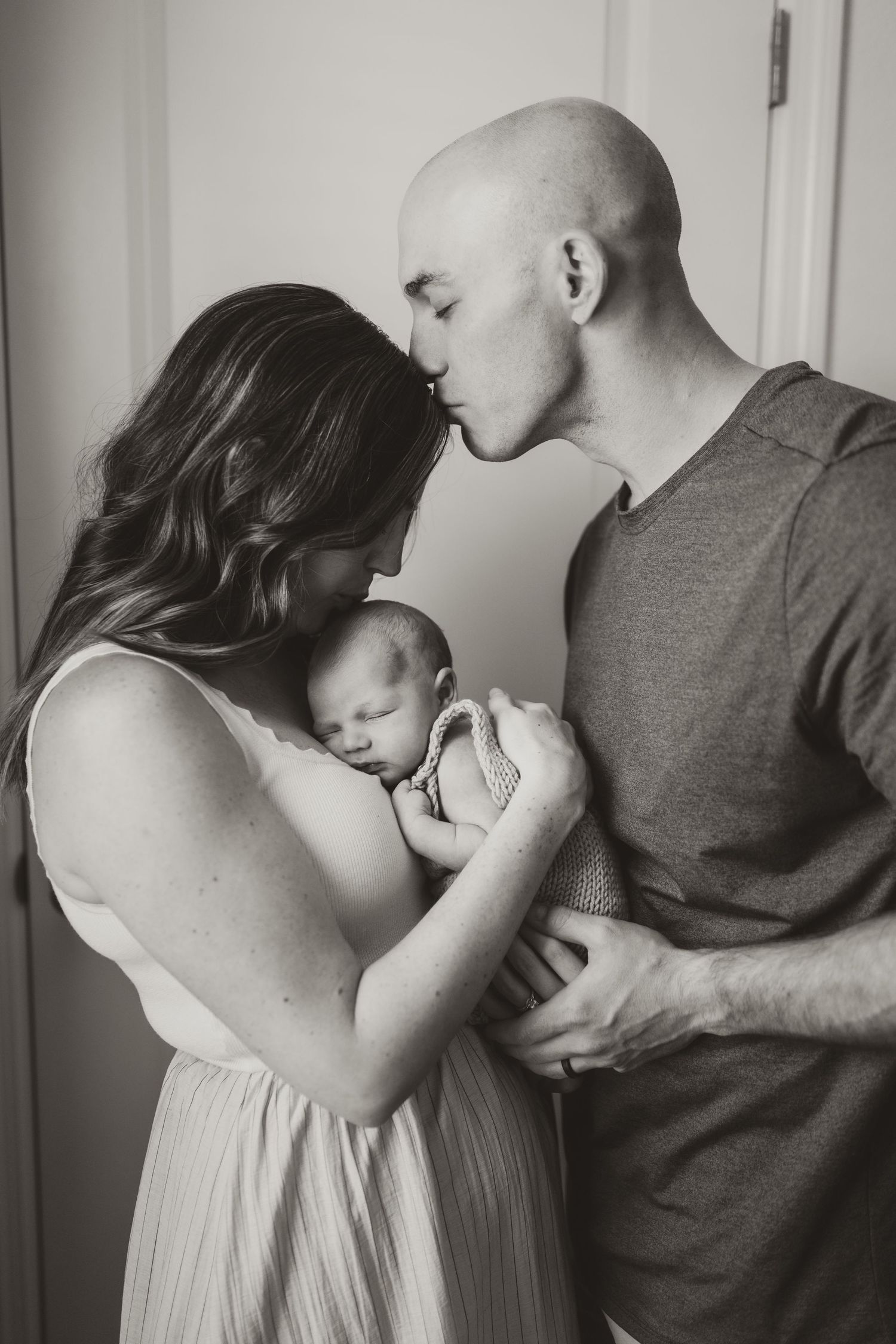 Intimate family photoshoot showing tender moments between parents and baby in black and white.