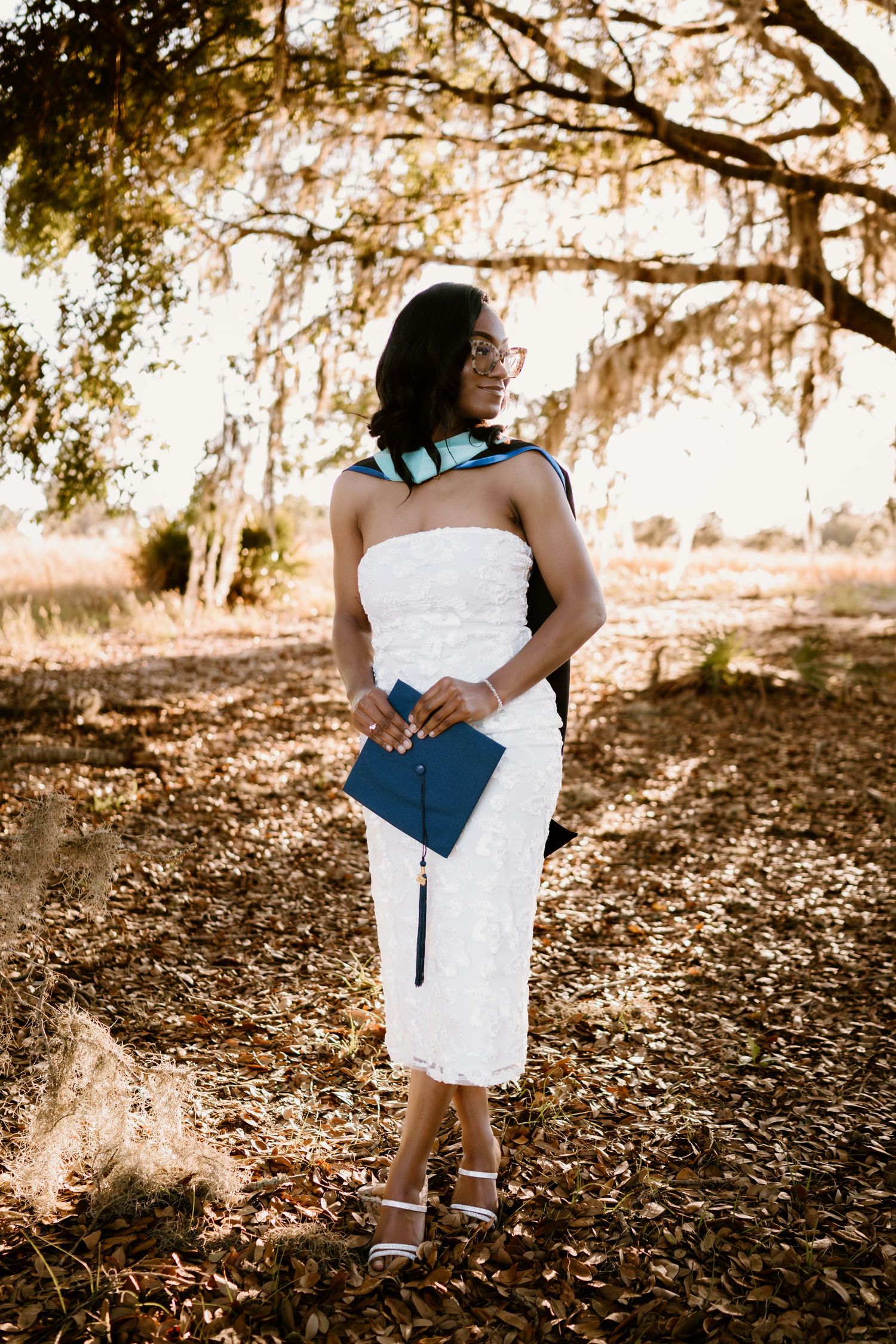 A romantic photoshoot under oak trees with filtered sunlight and fallen leaves.