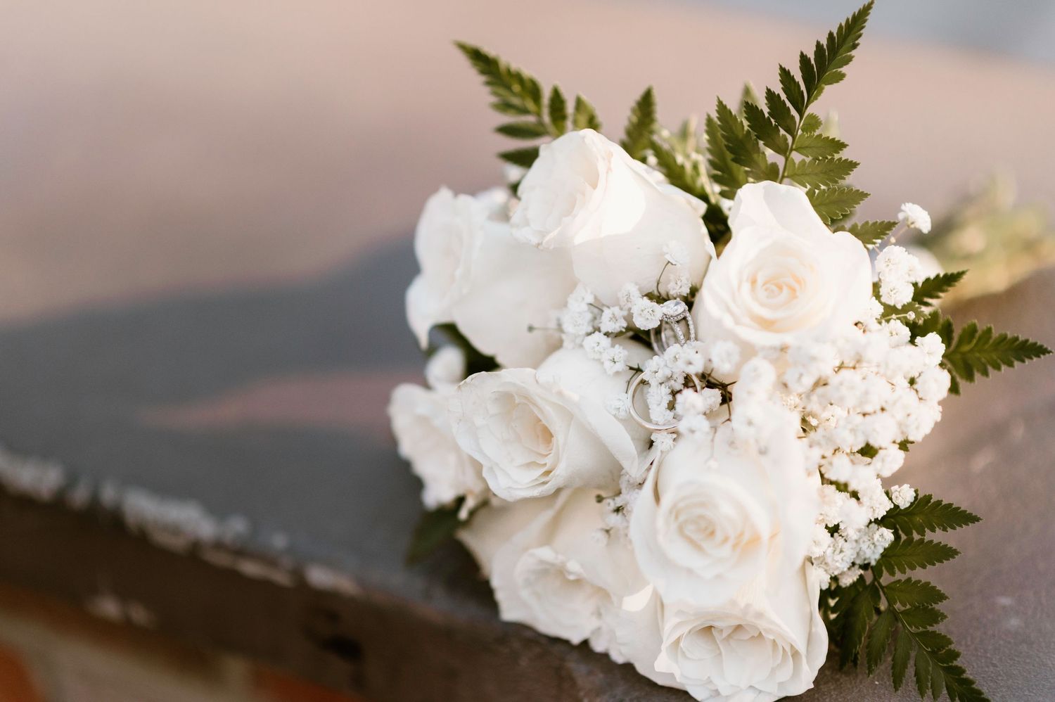 White roses and greenery bouquet arranged for a wedding against a blurred background.