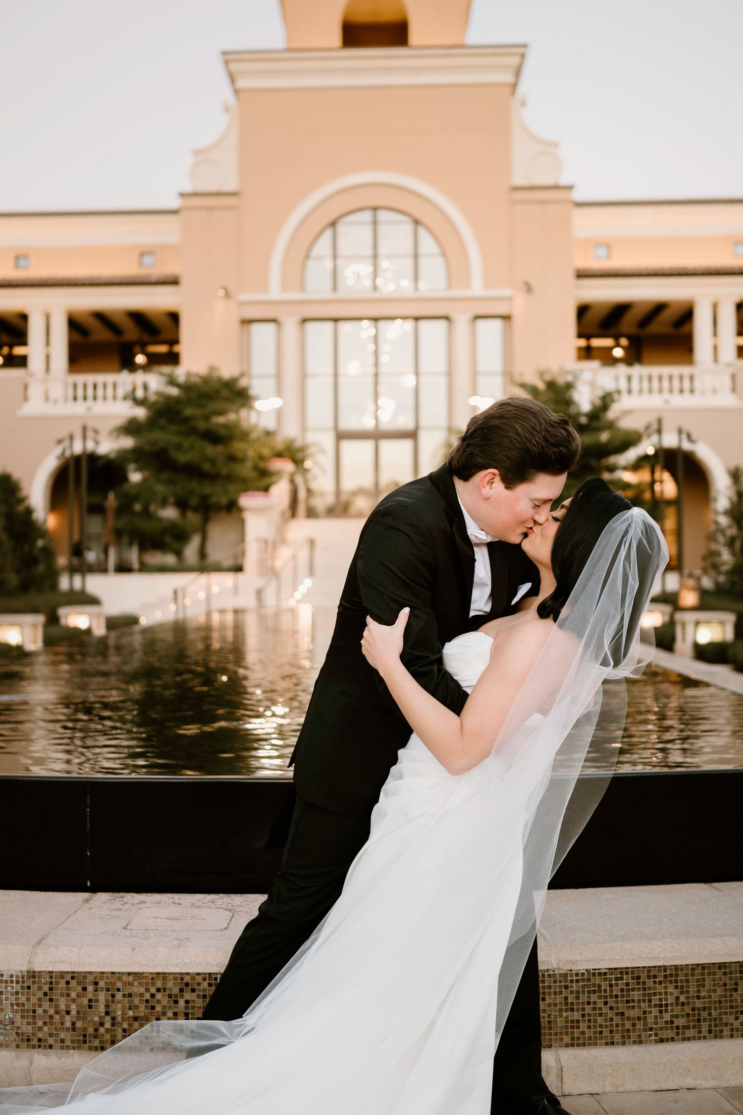 Romantic wedding kiss captured against elegant resort architecture.