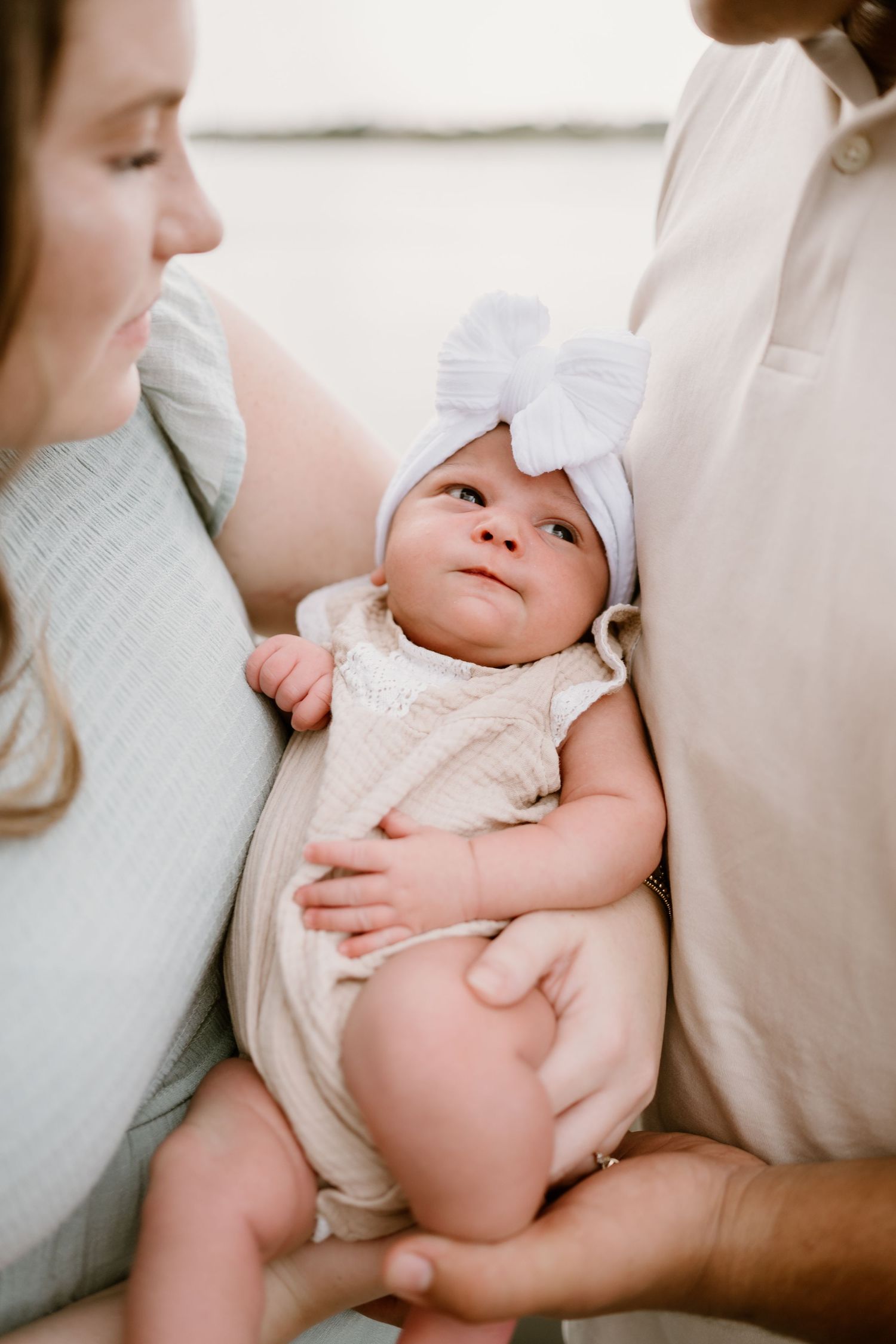 Close-up photo of a newborn baby wearing white clothing being held by parents.