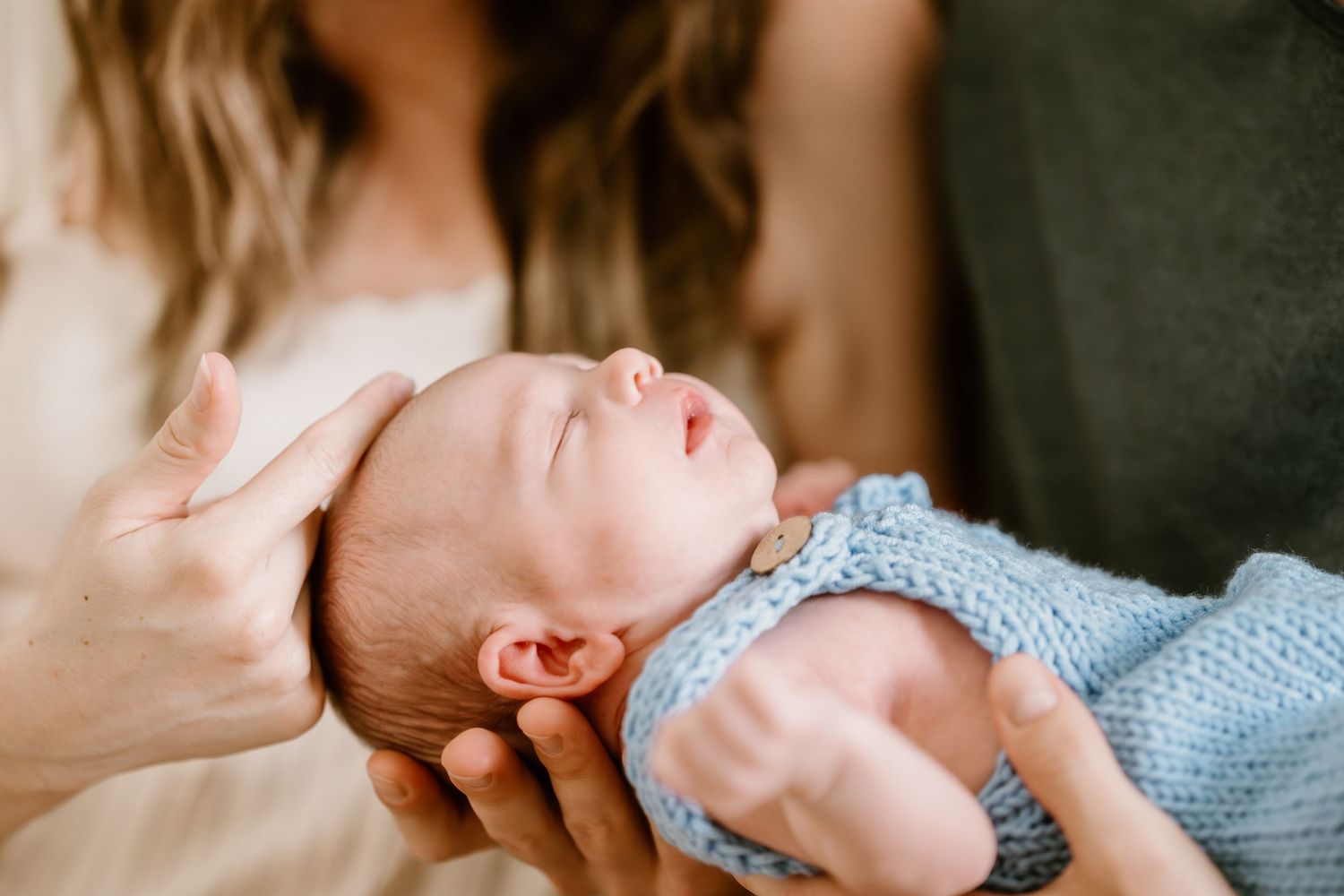 Close-up view of a sleeping infant in blue being gently cradled.