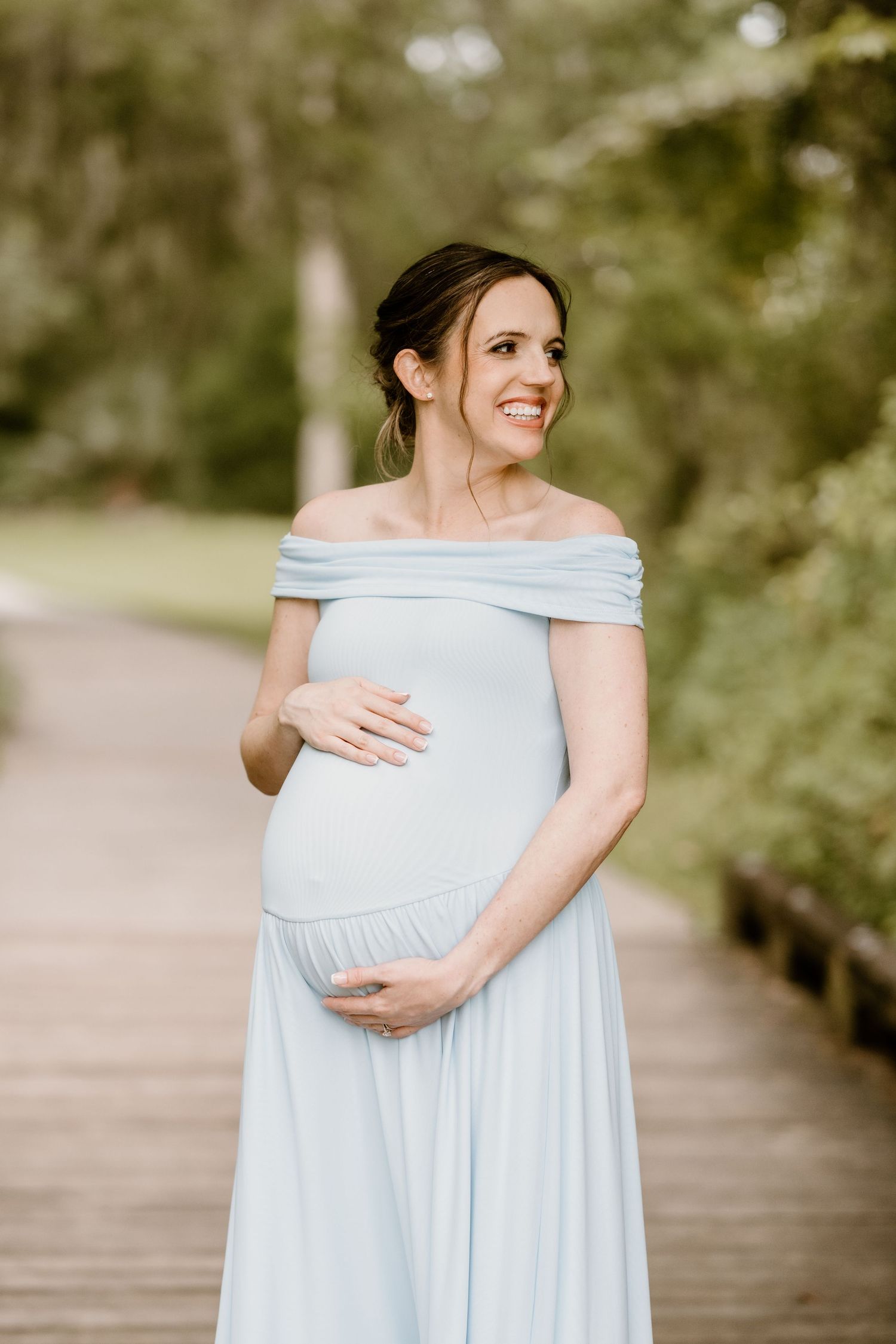 Maternity photos showing woman in light blue dress holding her baby bump.