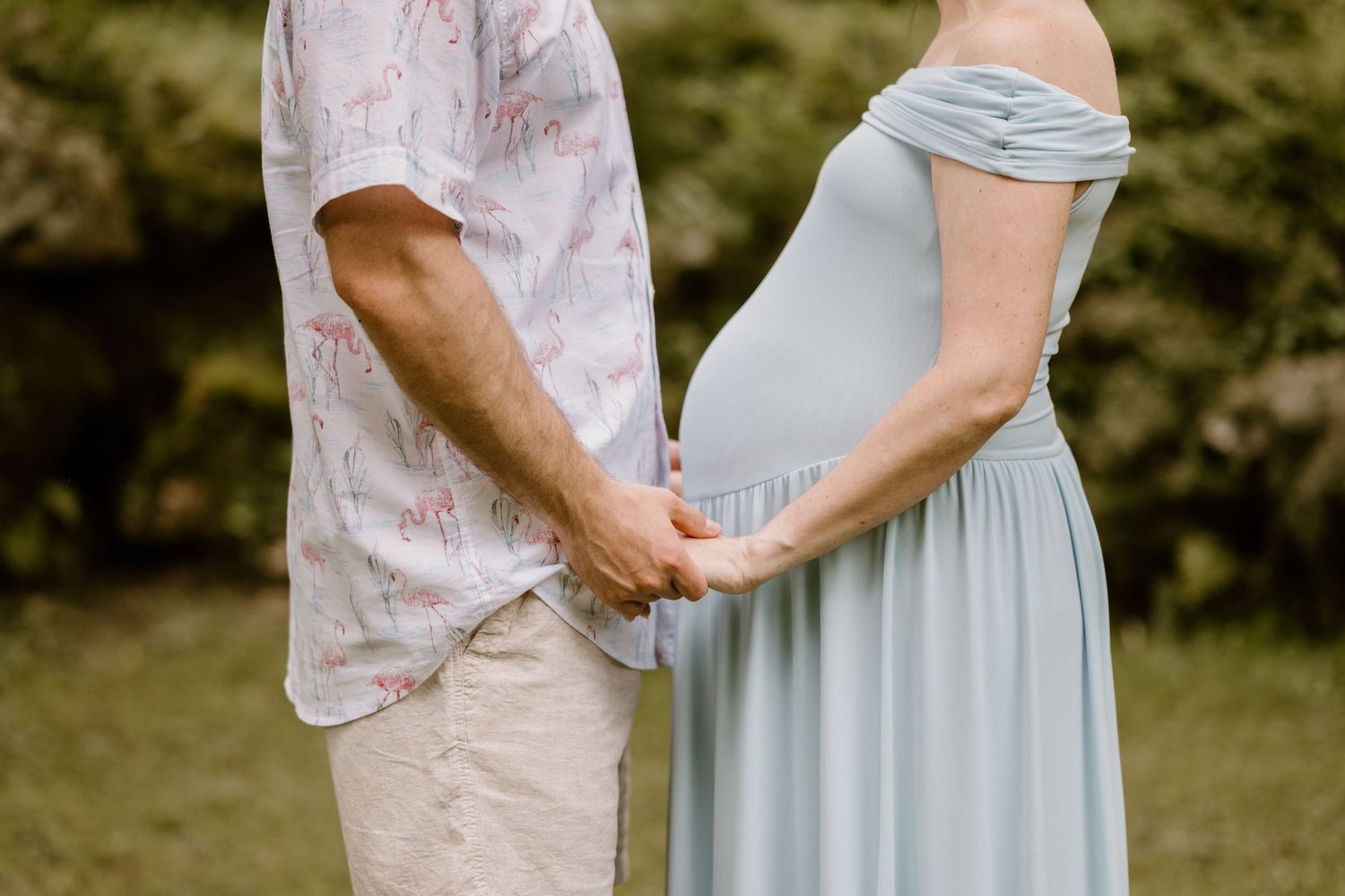 Close-up of couple holding hands with person wearing light blue maternity dress.