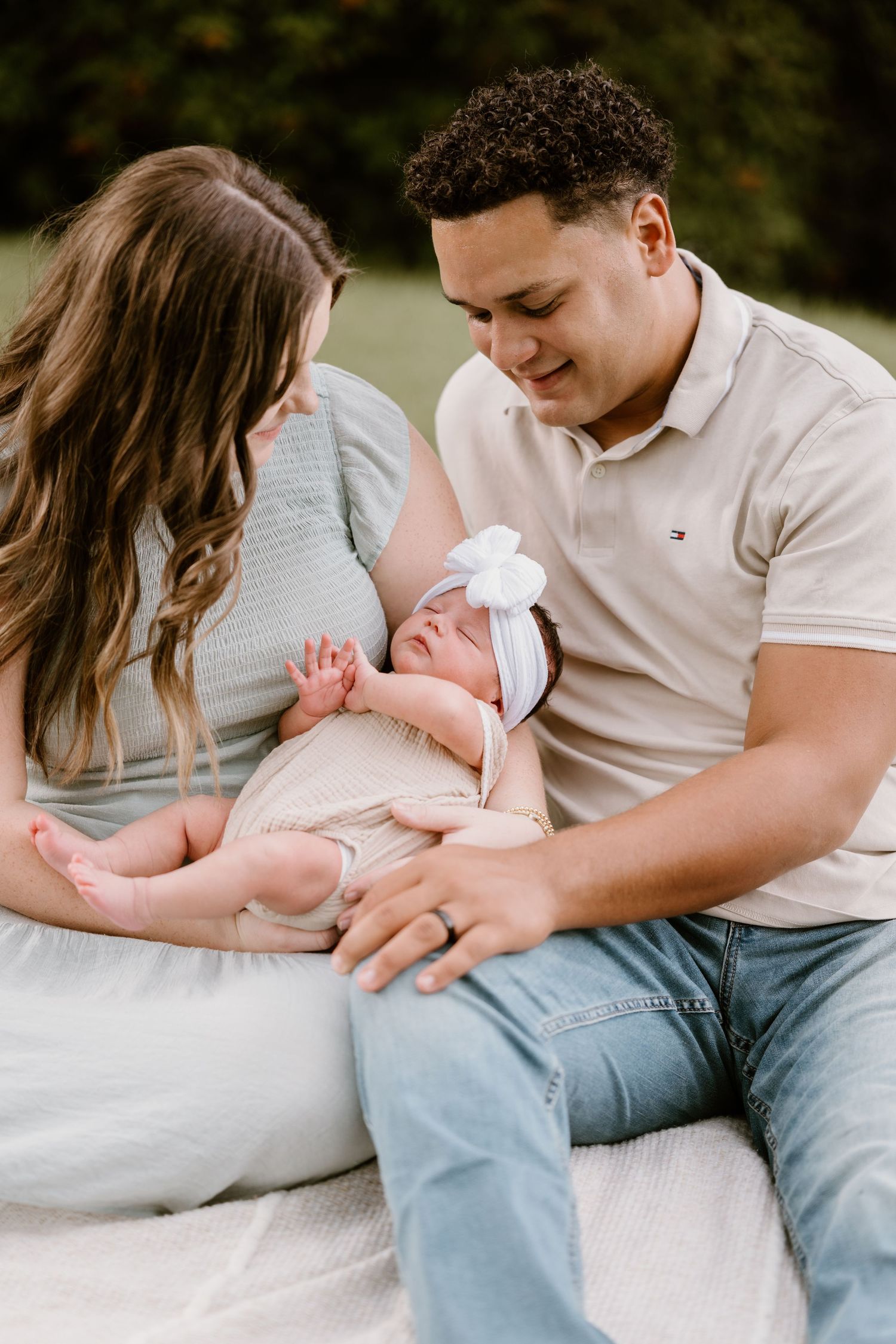 Candid family moment with parents holding their newborn baby in an outdoor setting.