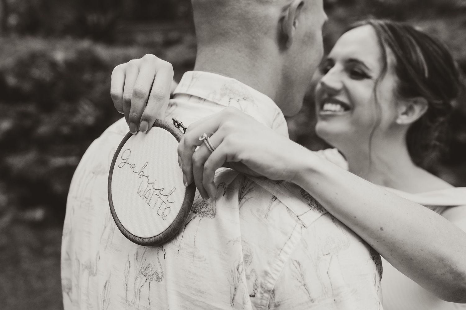 Black and white photo of couple sharing moment with embroidery hoop outdoors.