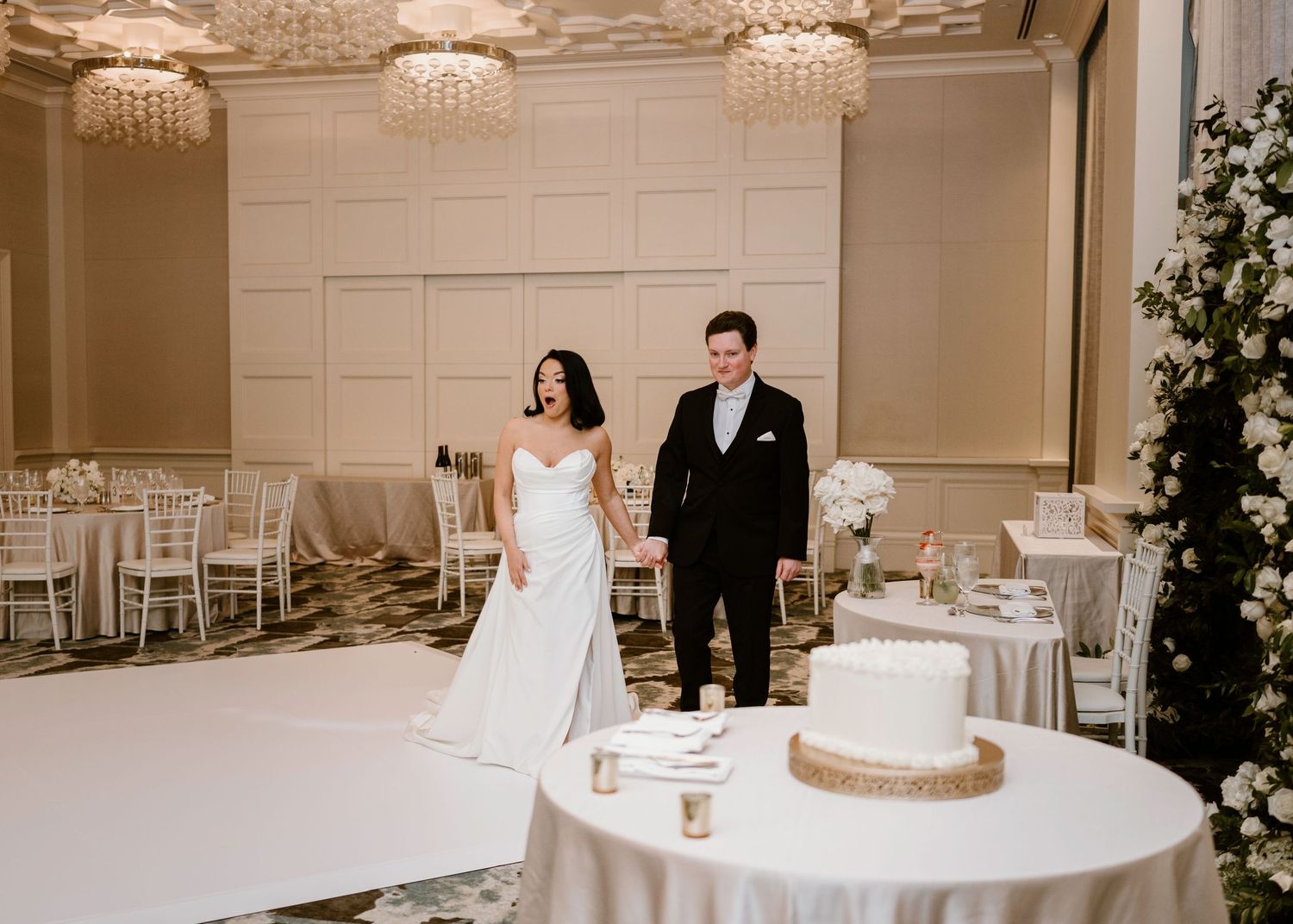 Elegant wedding reception hall with white tables and crystal chandeliers.